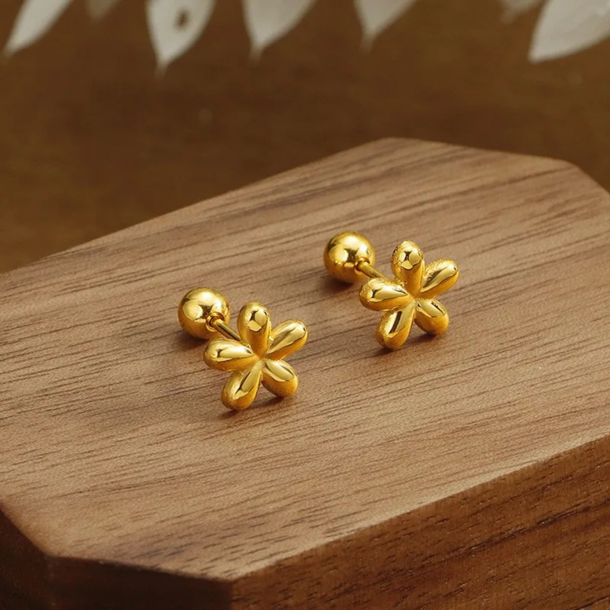 Gold flower-shaped earrings on a wooden surface