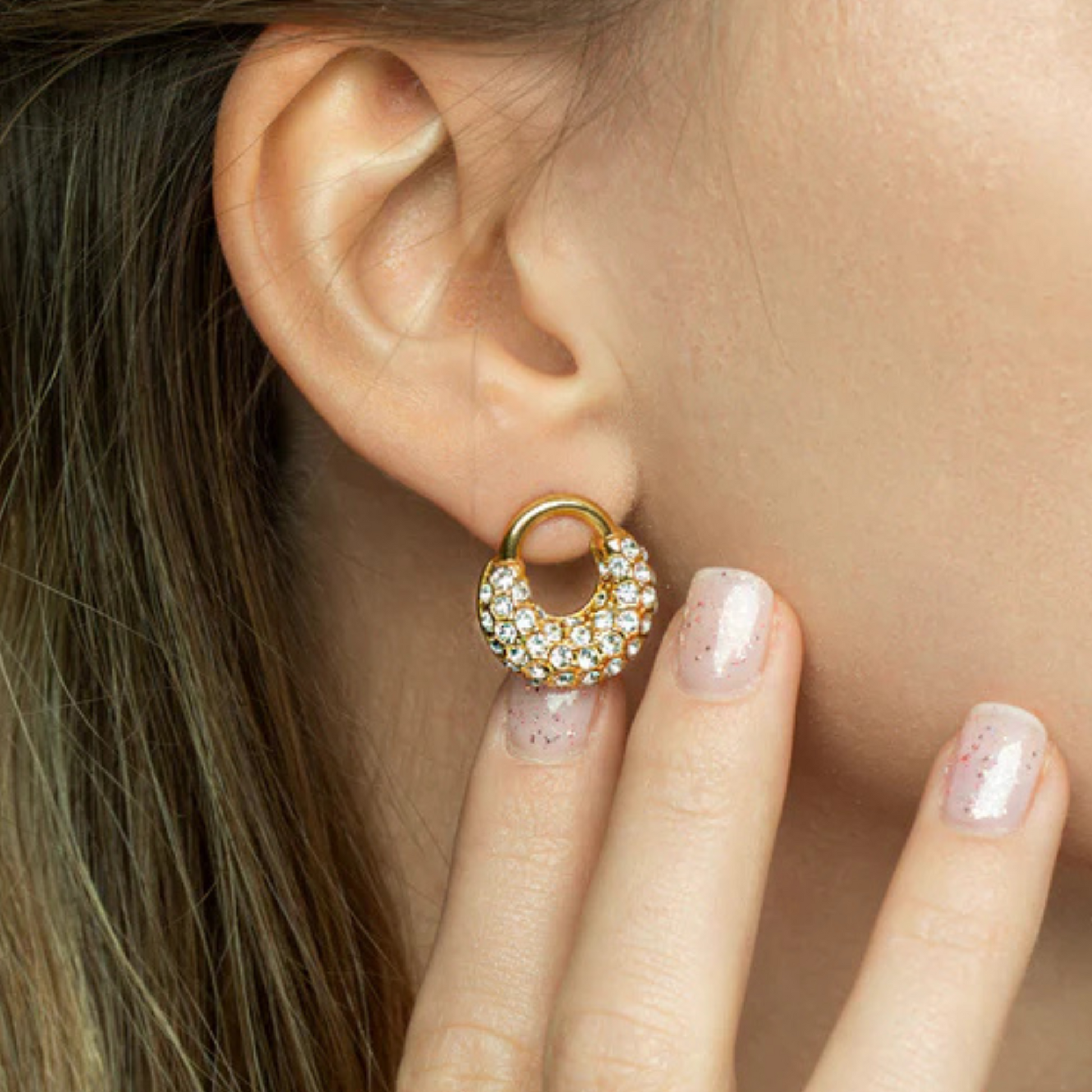 Close-up of a gold earring with small stones worn by a person.