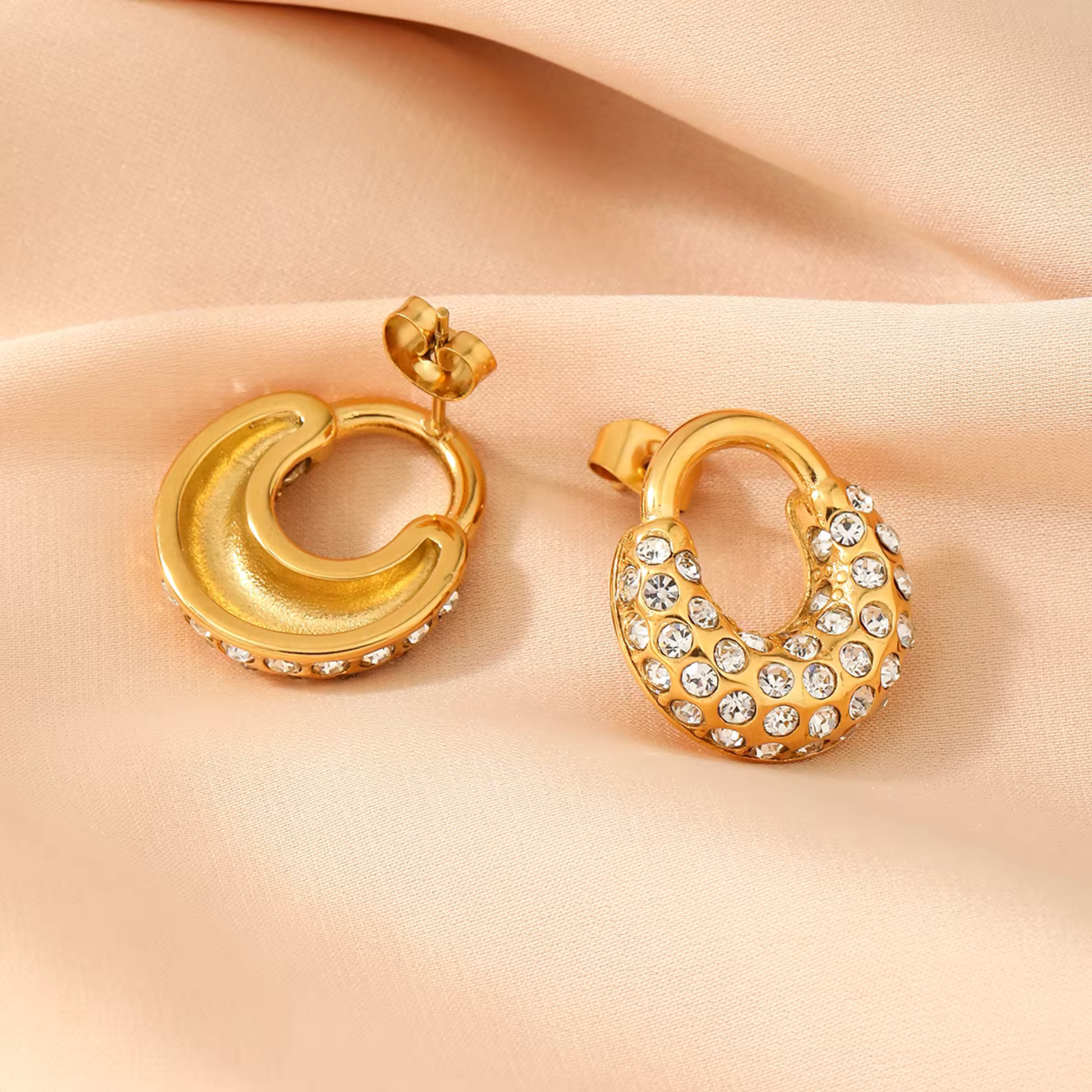 Gold hoop earrings with embedded crystals on a beige fabric background