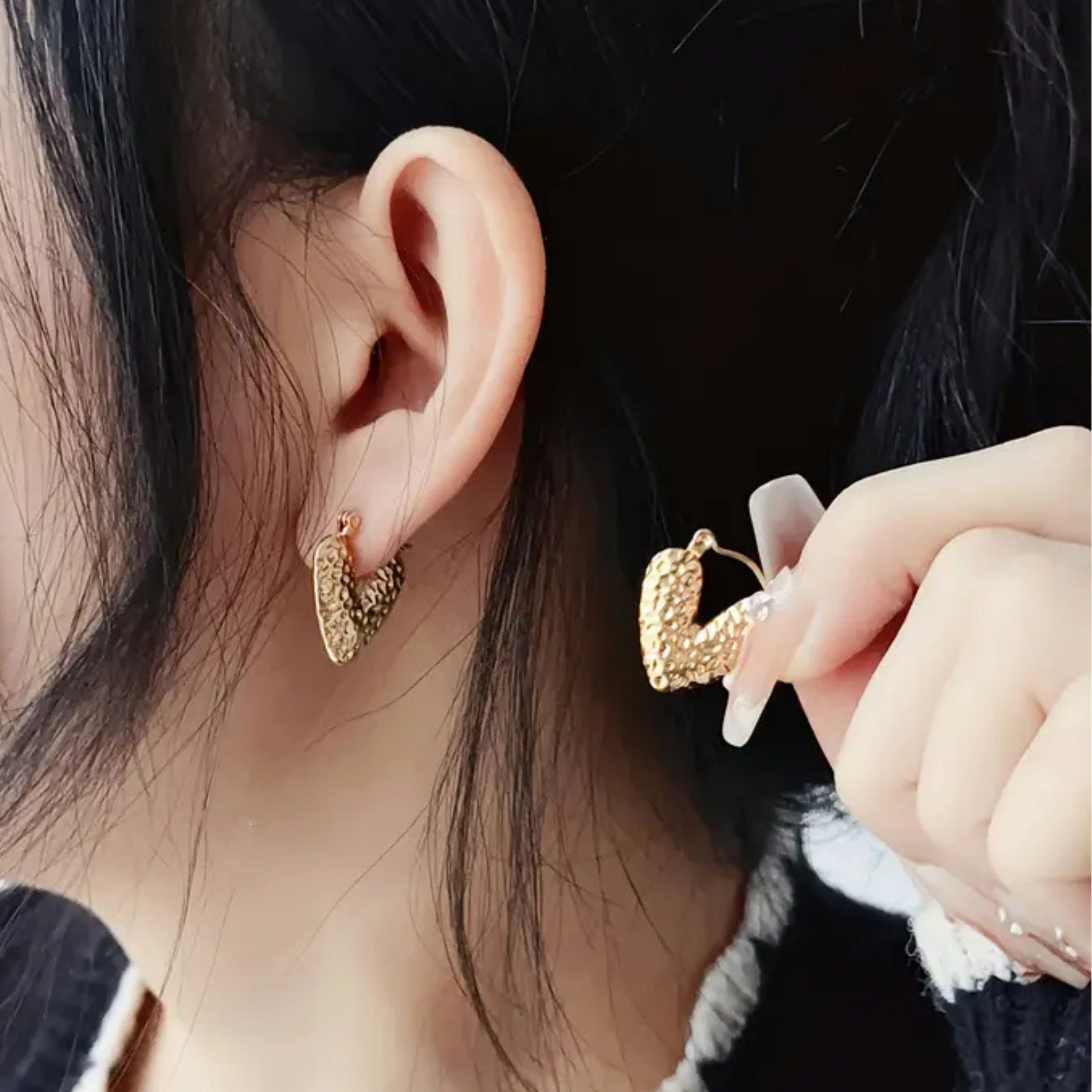 Gold heart-shaped earrings being worn and held by a person.