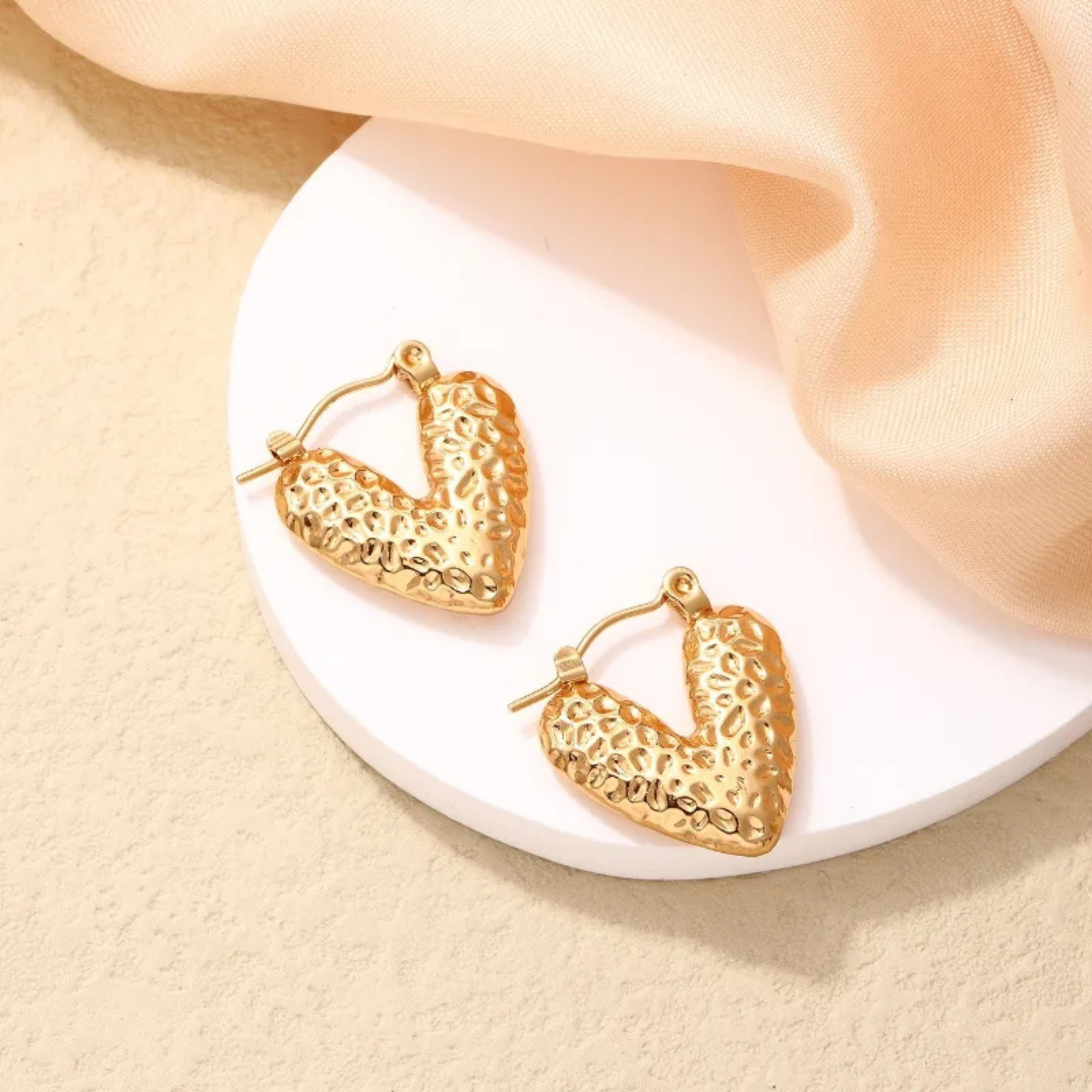 Gold hoop earrings on a white plate with beige fabric background