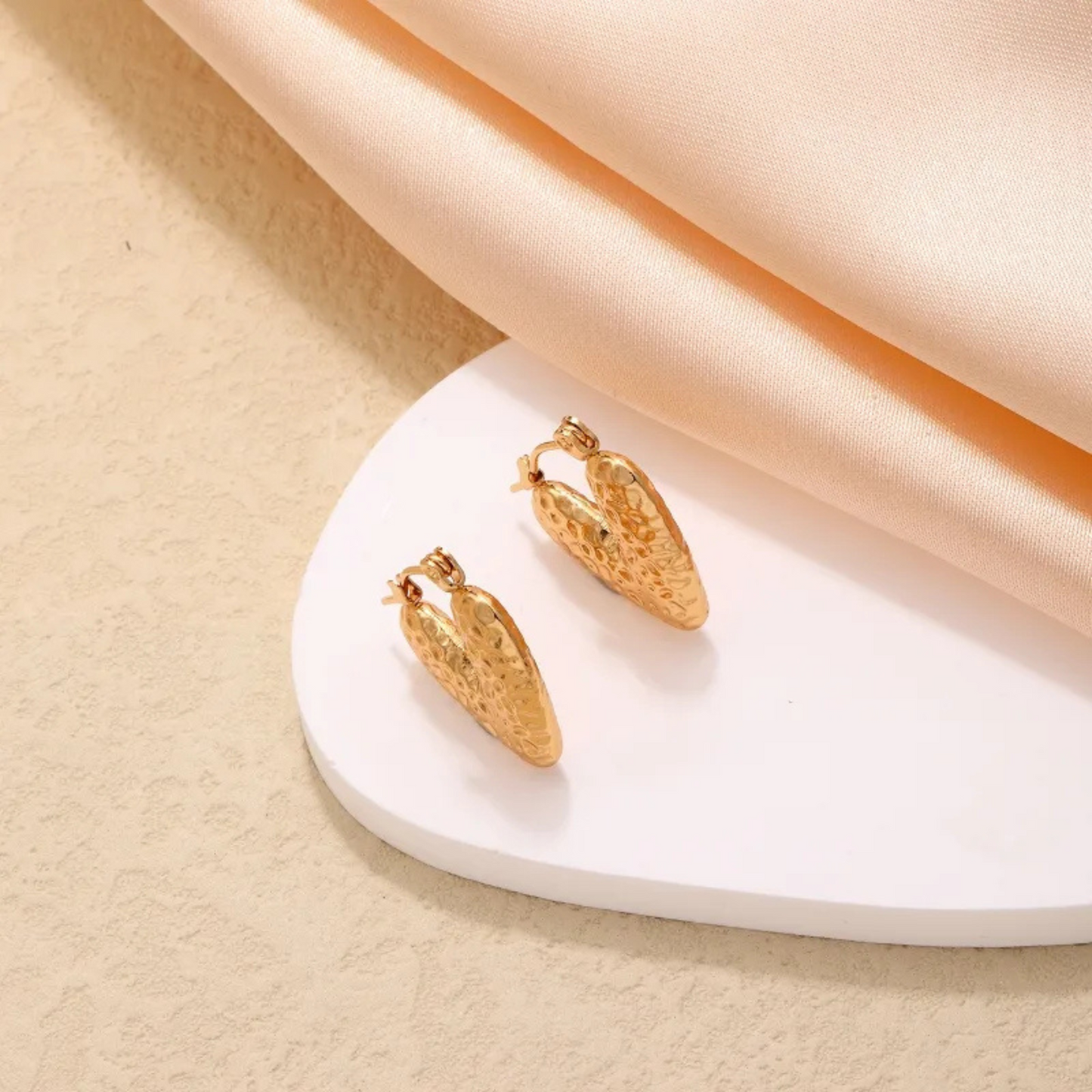 Gold earrings on a white stand with a beige background