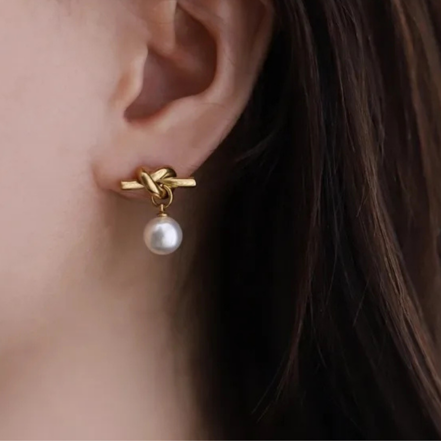 Gold earring with a pearl on an ear against a neutral background