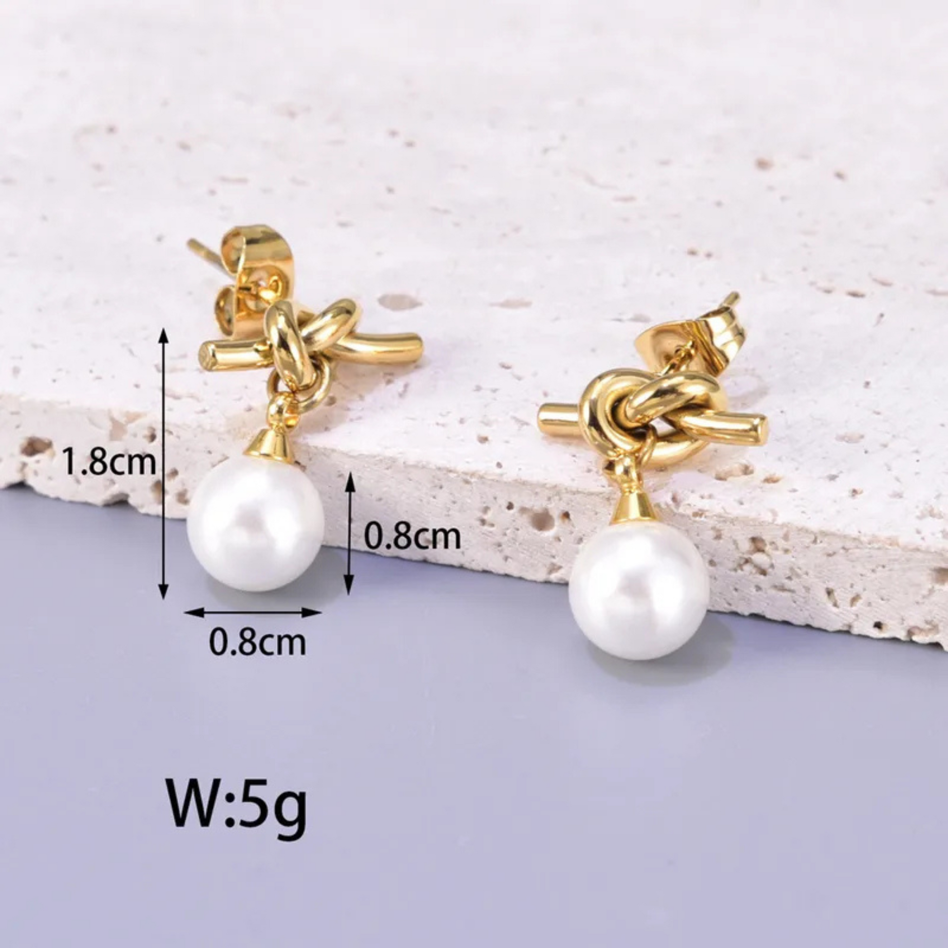 Gold earrings with pearls on a textured surface, showing measurements.