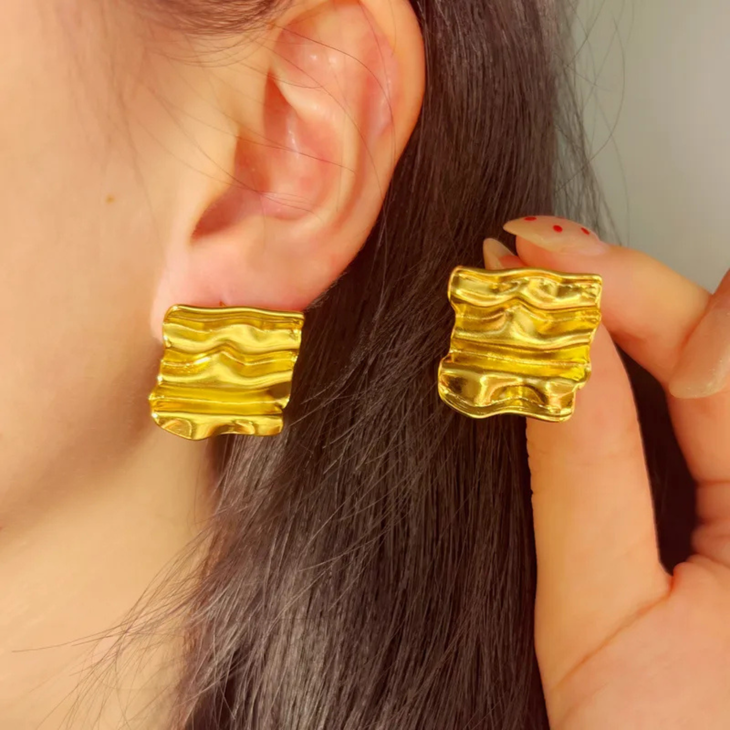 Gold earrings being worn and held by a person with dark hair.