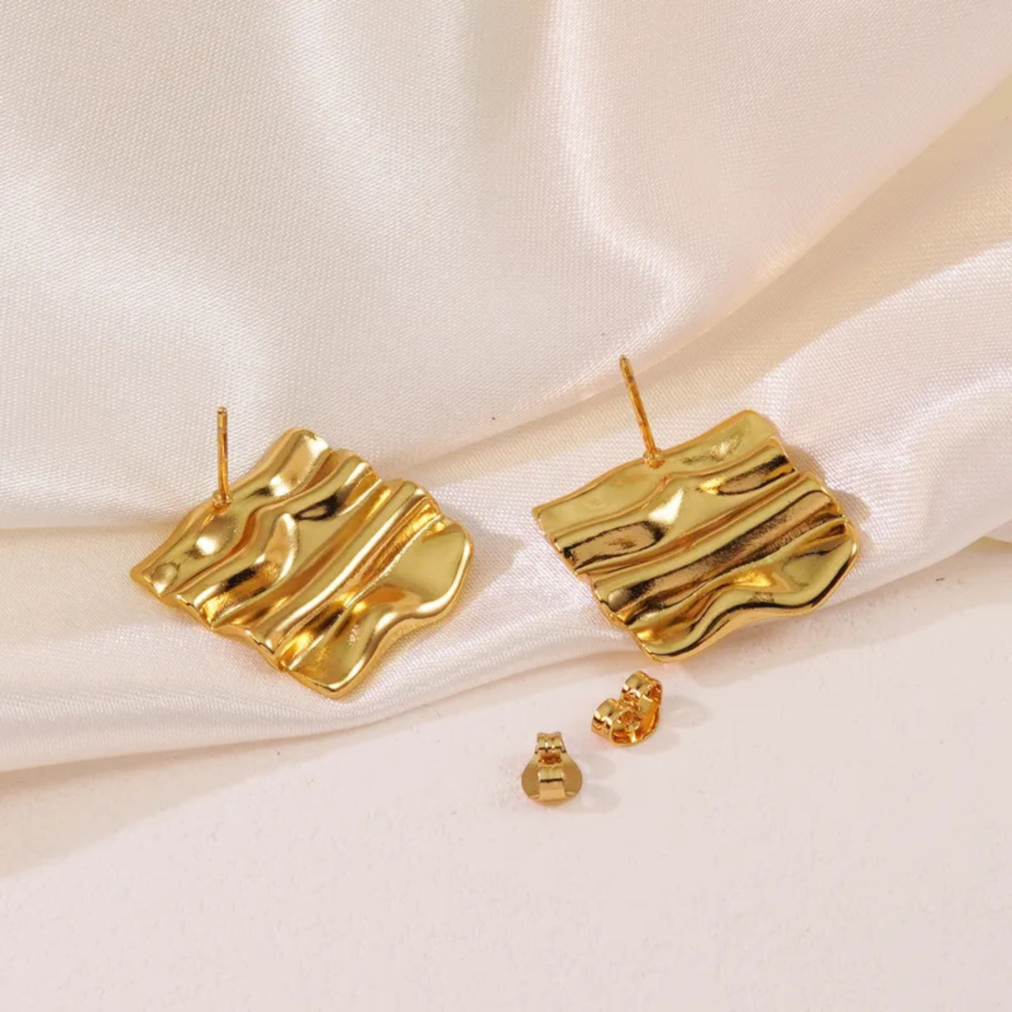 Gold earrings on a white satin background