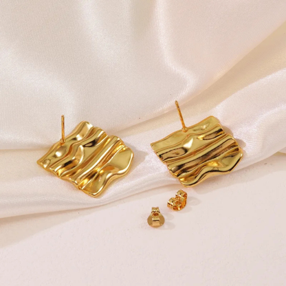 Gold earrings on a white satin background