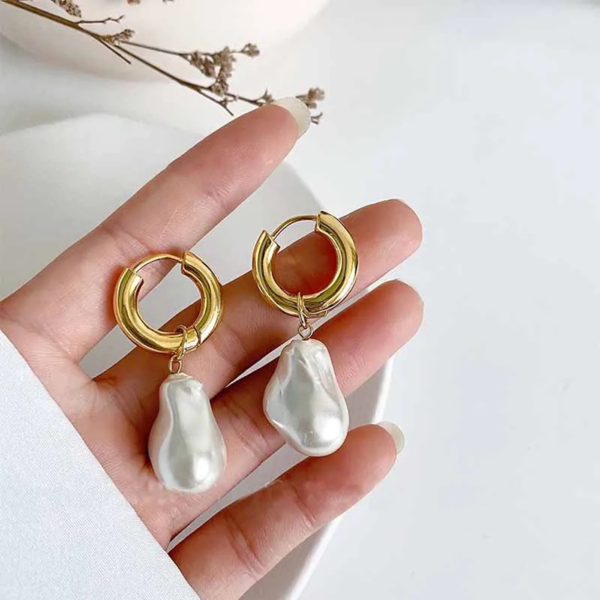 Gold hoop earrings with pearl drops held in a hand against a white background