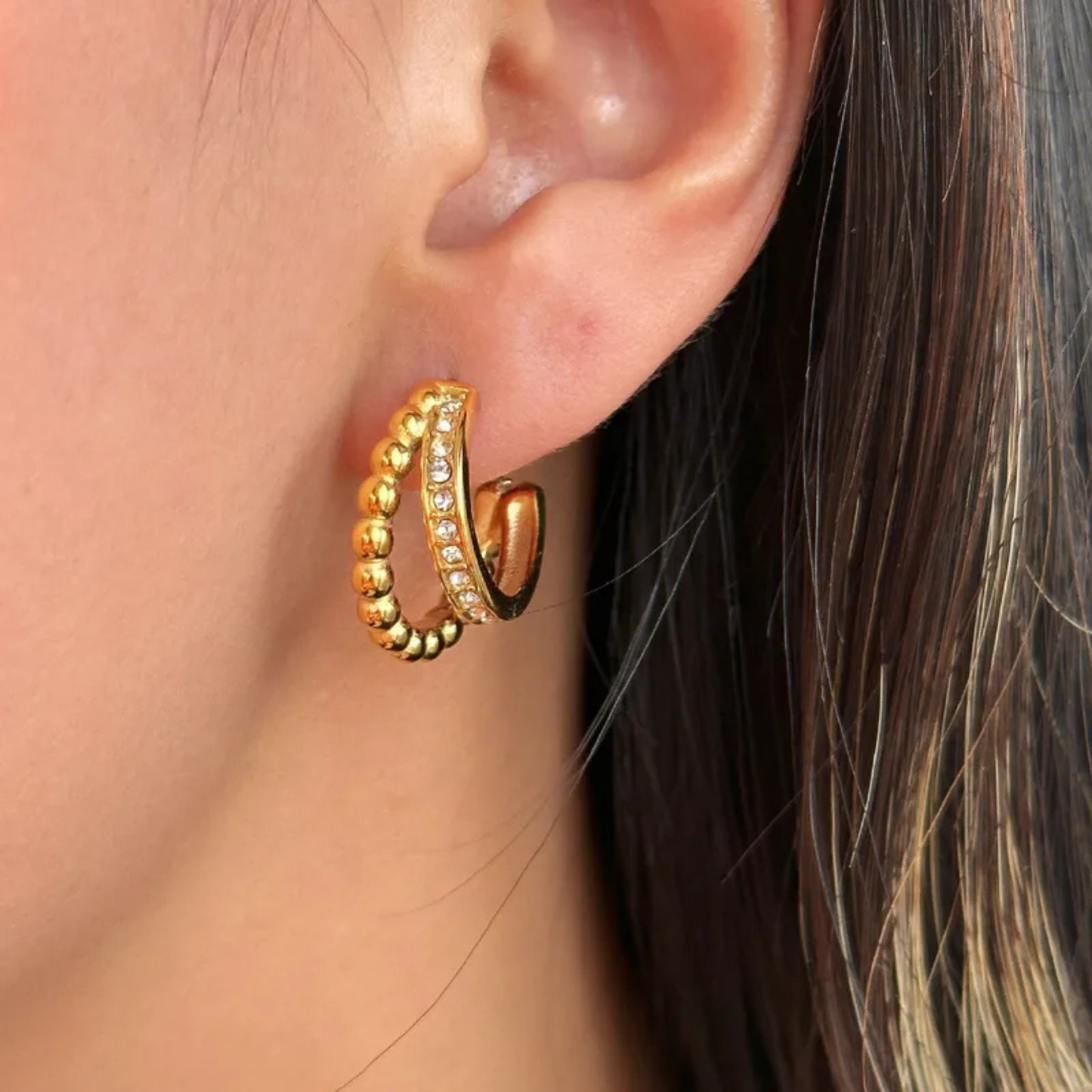 Gold hoop earring with embedded stones worn by a person.