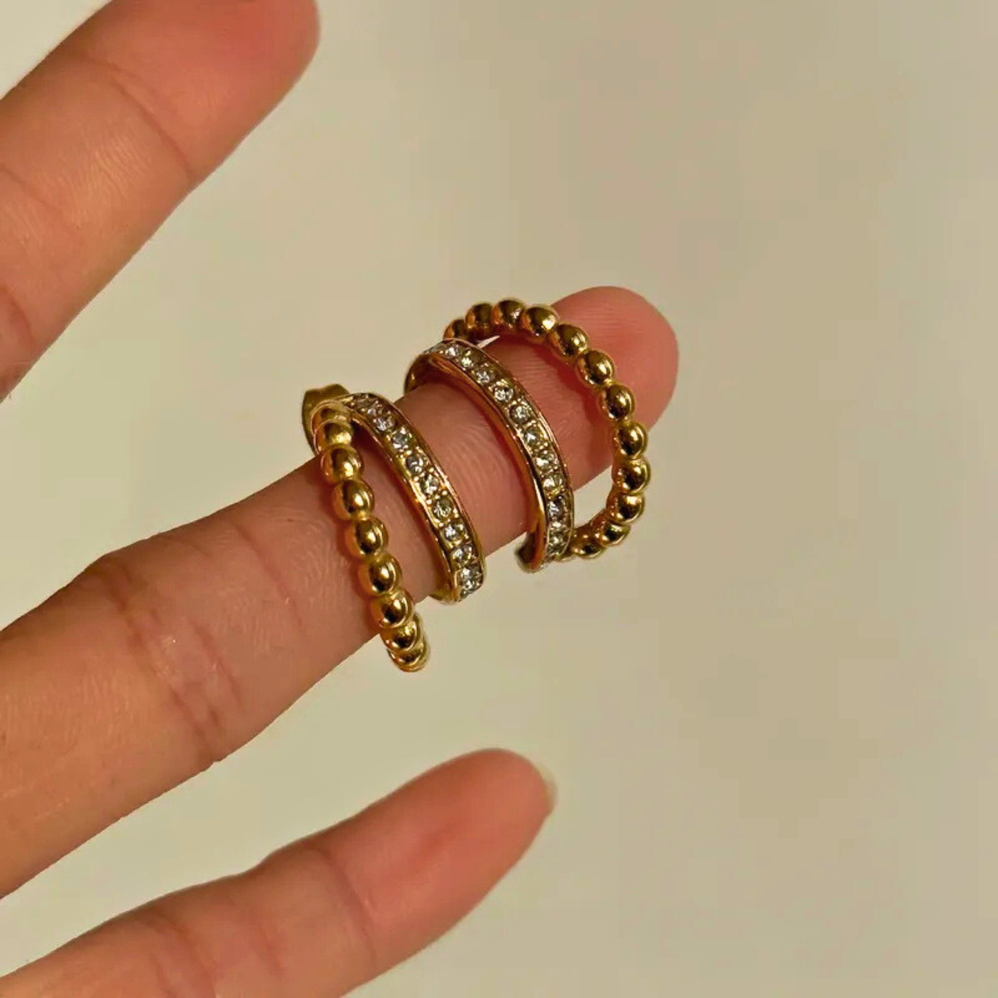 gold earrings on a finger against a plain background