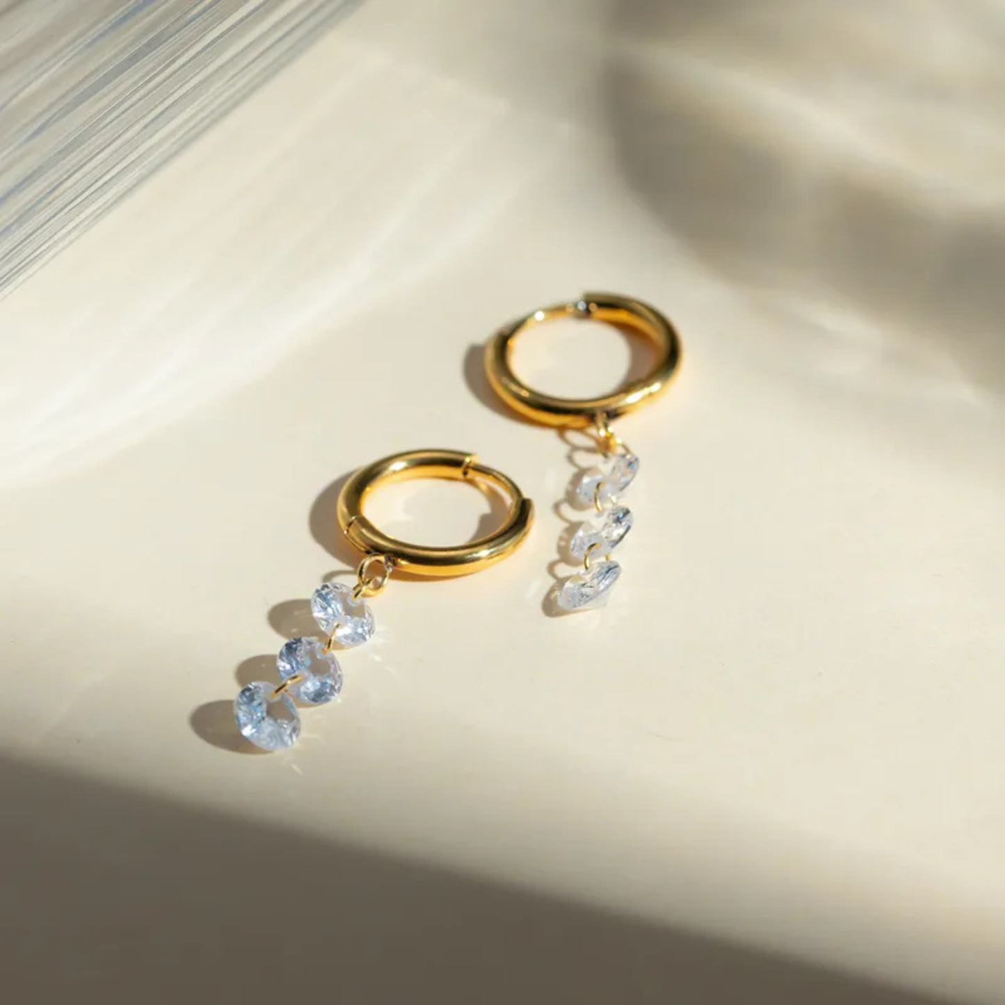 Gold hoop earrings with crystal drops on a light background