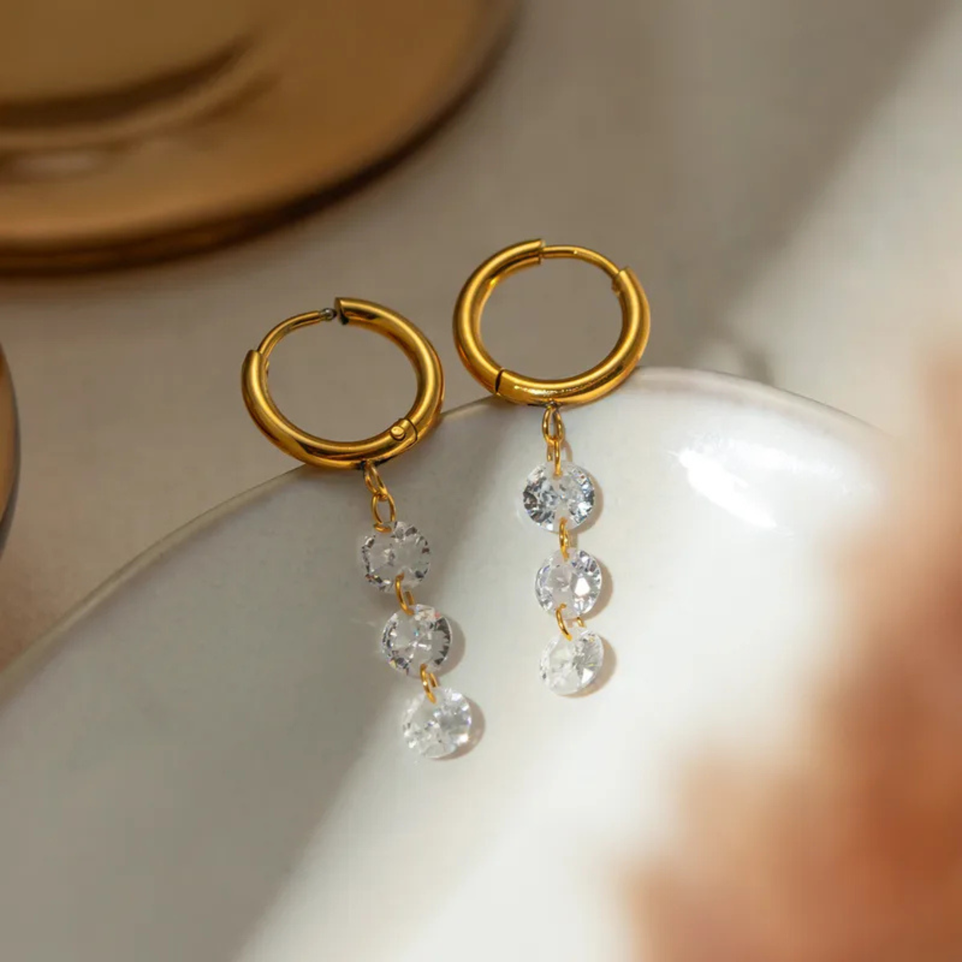 Gold hoop earrings with crystal drops on a white surface