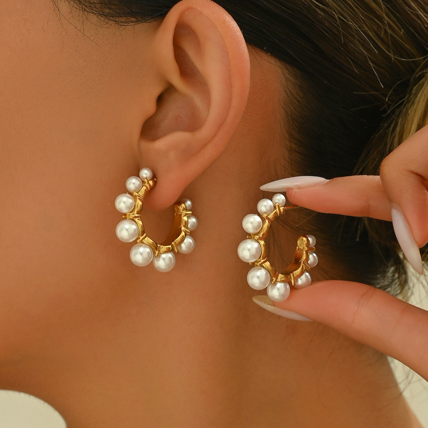 Pearl hoop earrings being worn and adjusted by a hand.