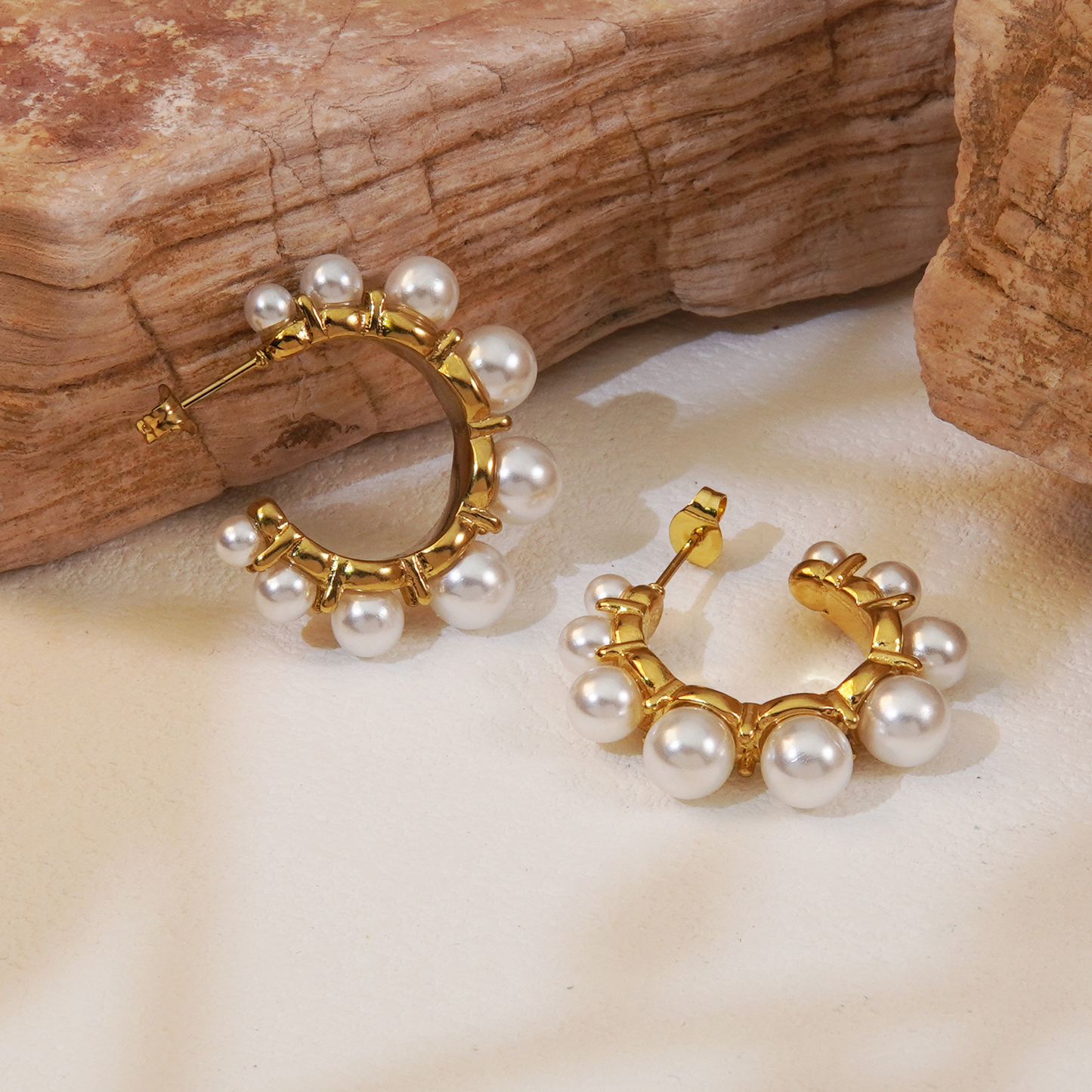 Gold hoop earrings with pearls on a natural wood and stone background