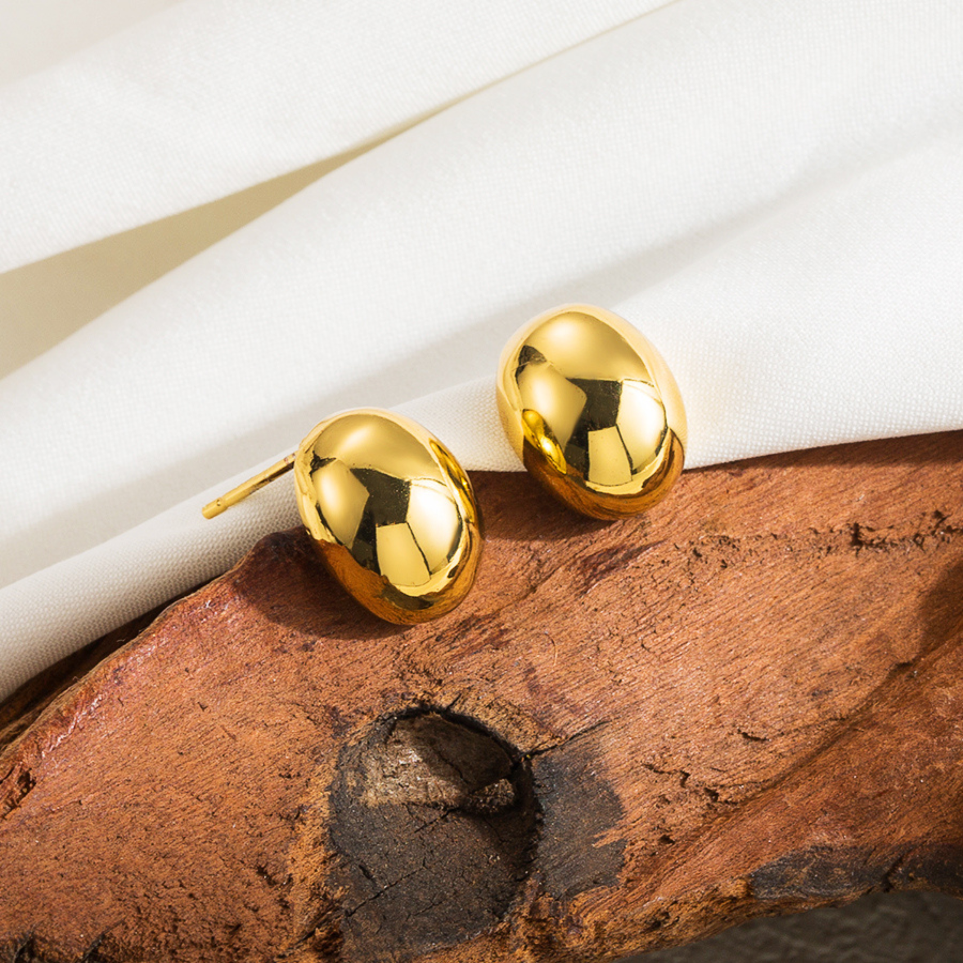 Gold earrings on a wooden surface with white fabric in the background