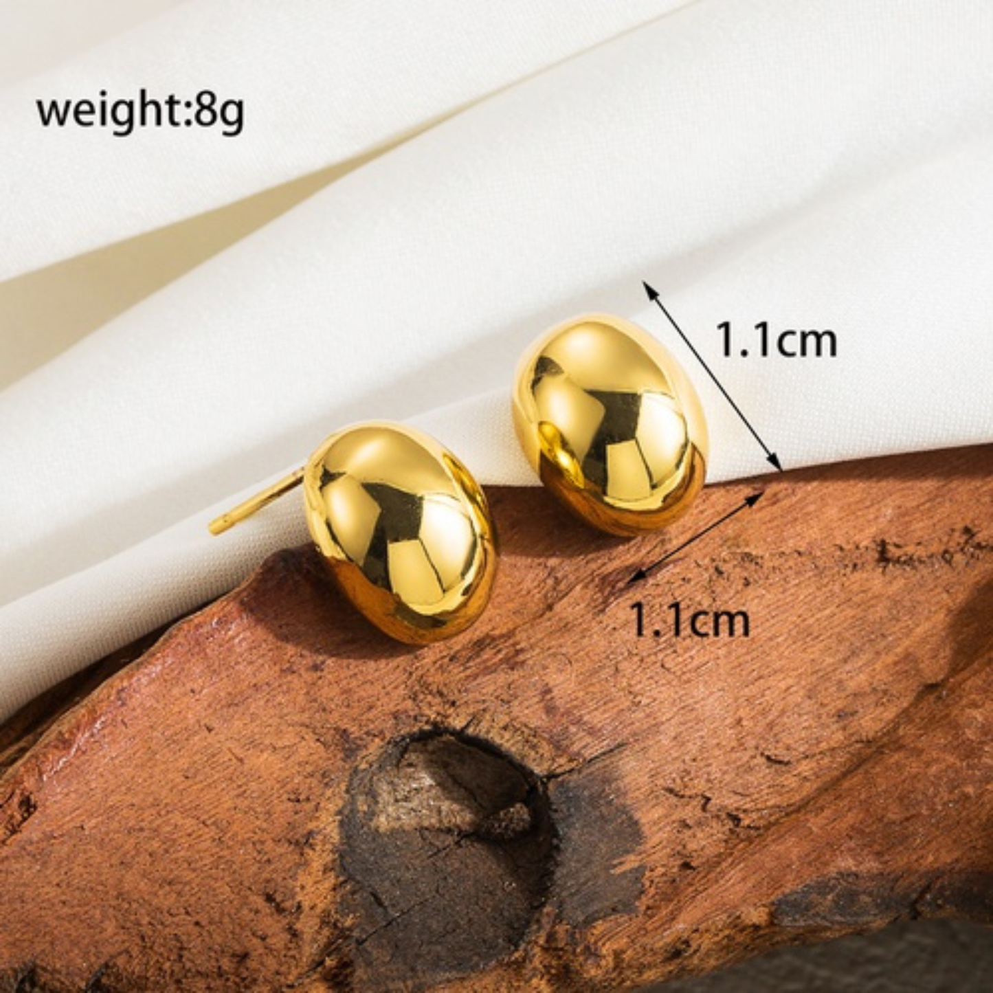 Gold earrings on a wooden surface with measurements and weight information.
