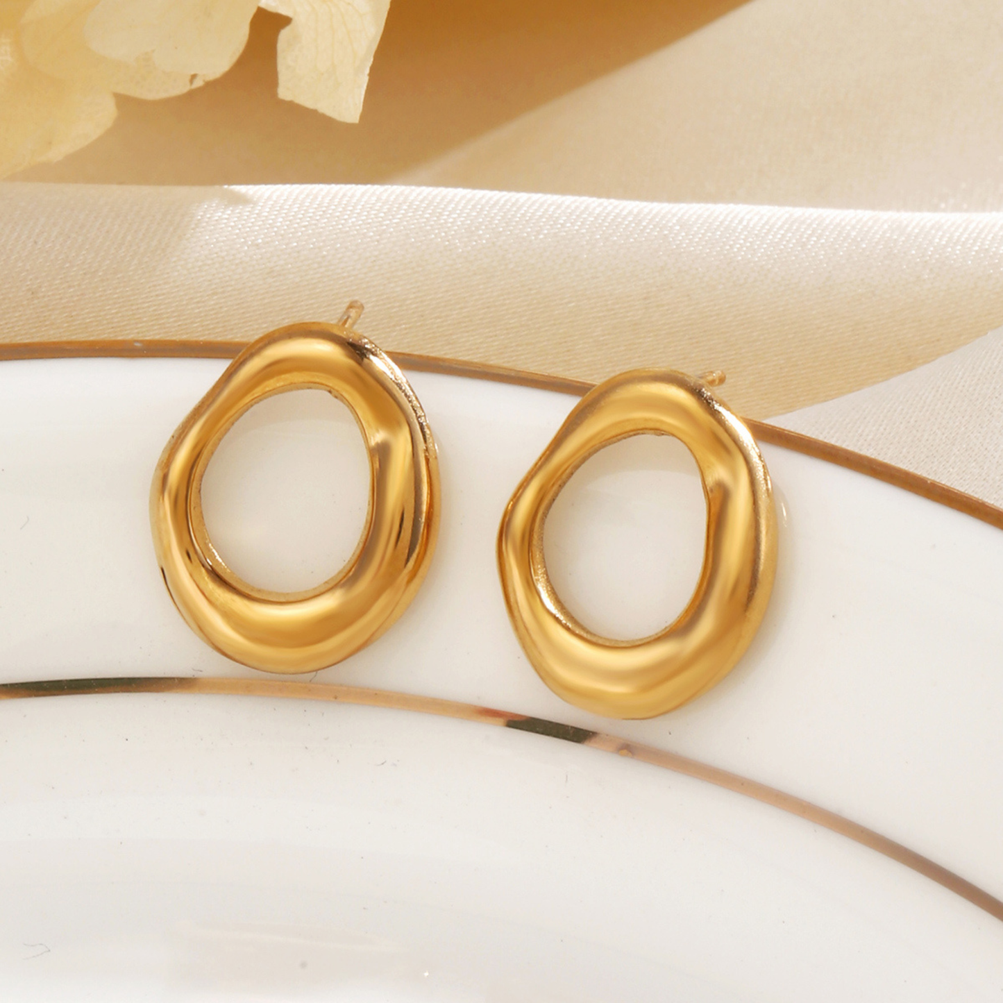 Gold stud earrings on a white plate with a beige background