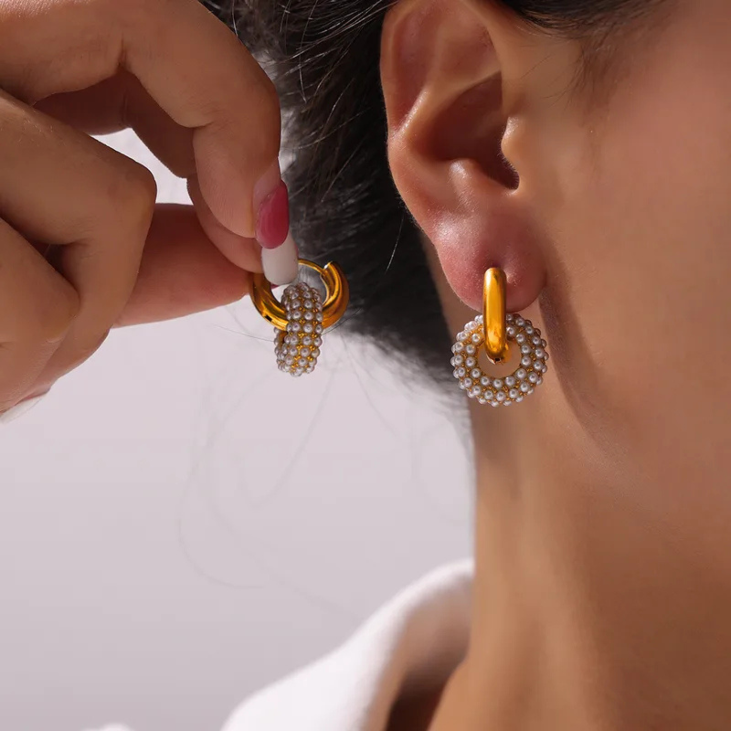 Gold hoop earrings with pearl-like beads being worn by a person.