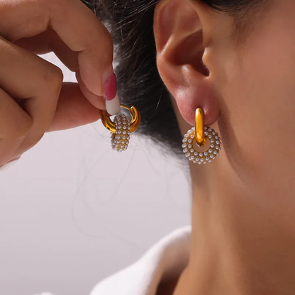 Gold hoop earrings with pearl-like beads being worn by a person.