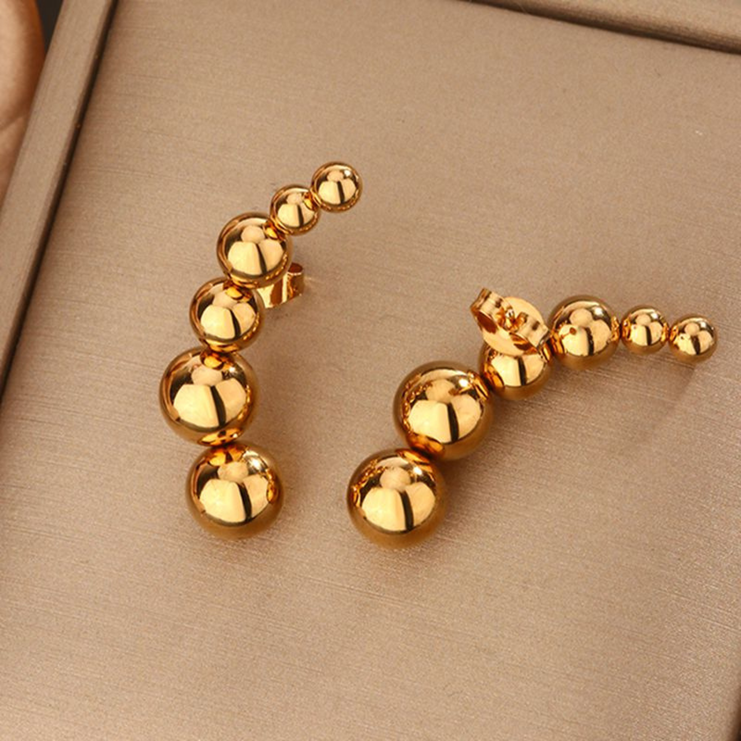 Gold beaded earrings on a beige background