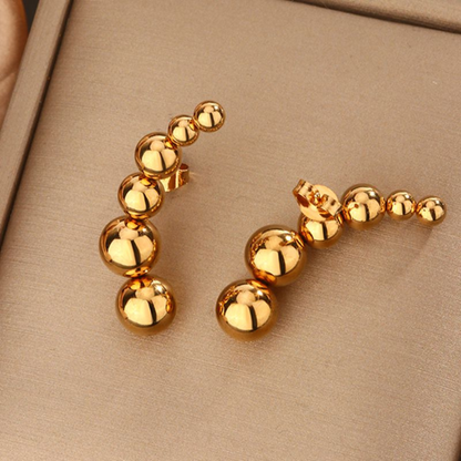 Gold beaded earrings on a beige background