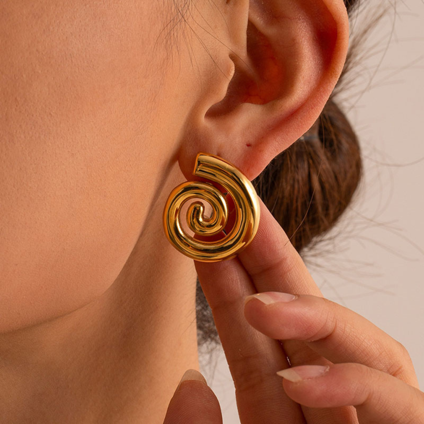 Gold spiral earring worn by a person with a neutral background