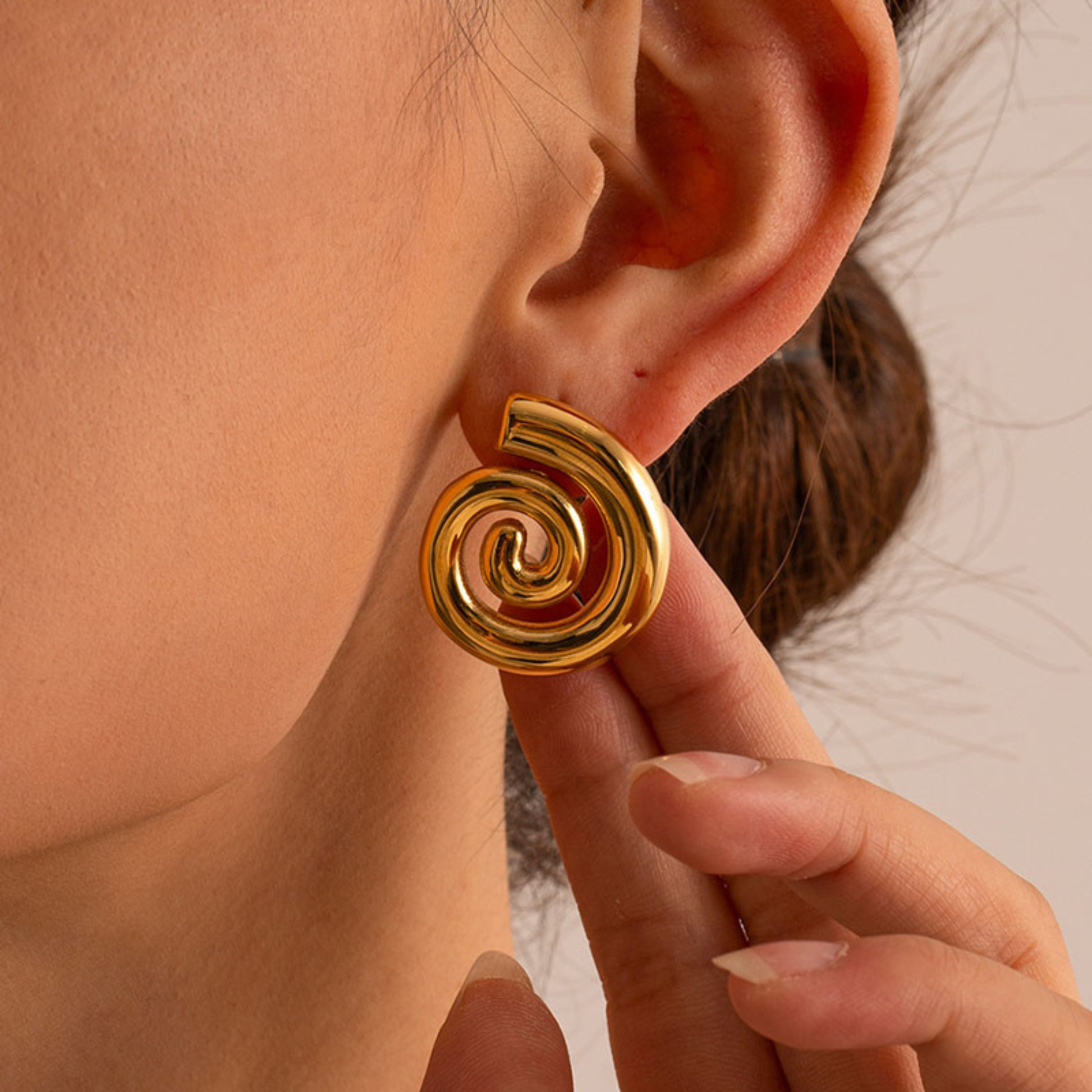 Gold spiral earring worn by a person with a neutral background