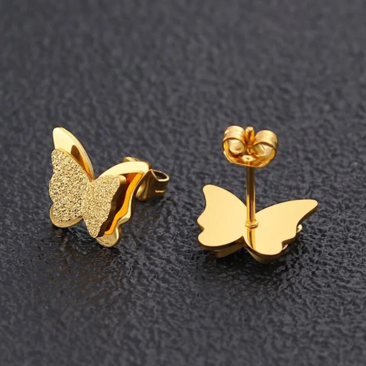 Gold butterfly earrings on a black textured background