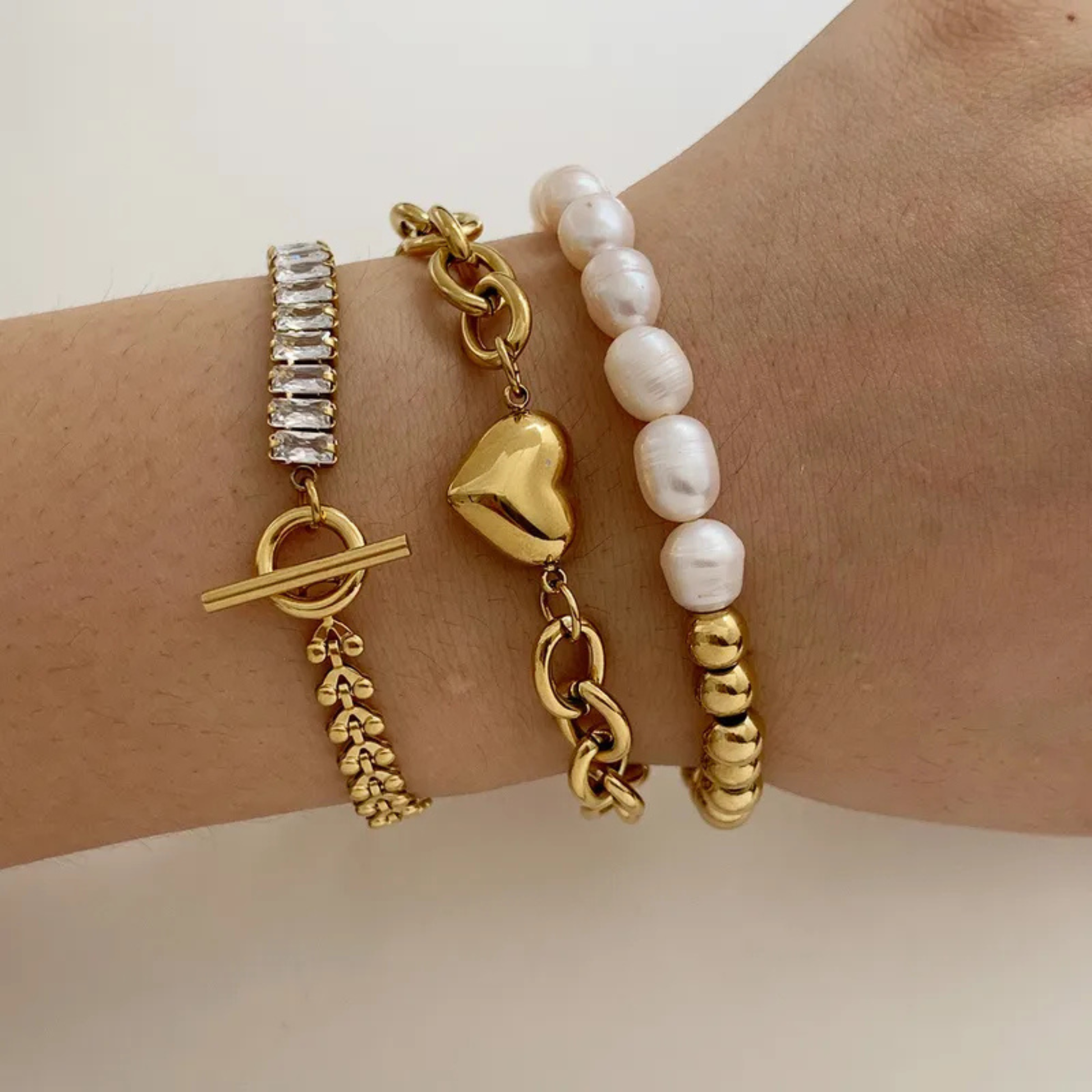 Wrist wearing multiple gold and pearl bracelets on a neutral background