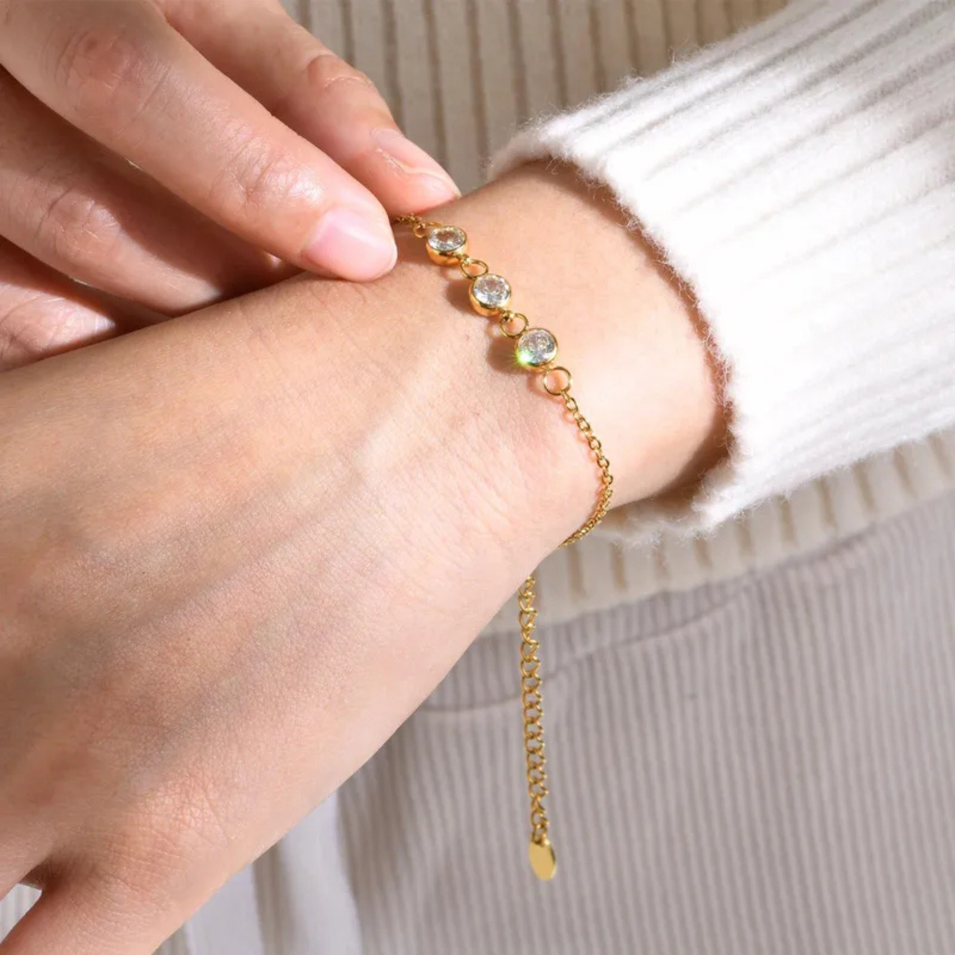 Gold bracelet with small stones on a wrist against a neutral background