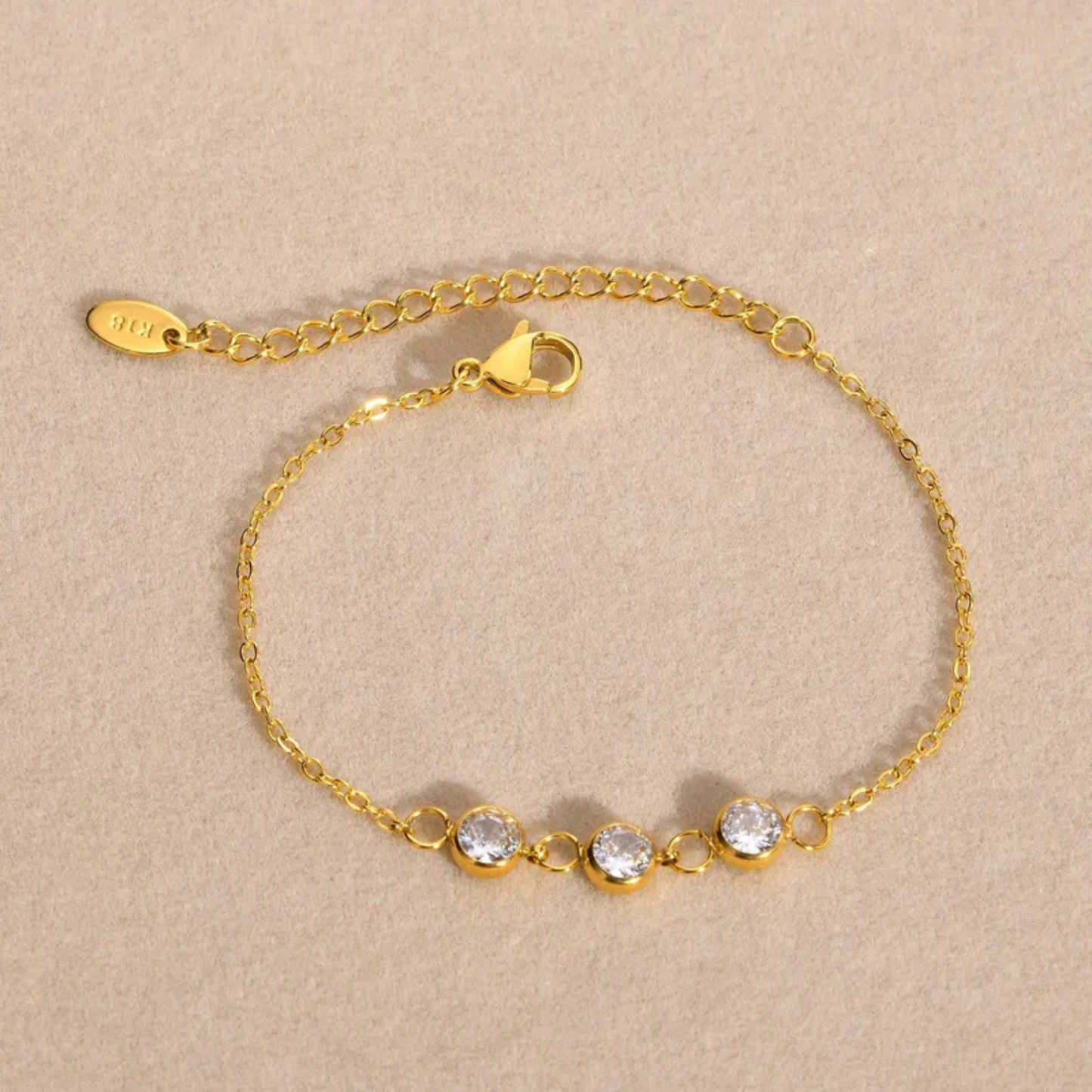 Gold bracelet with three clear stones on a beige background