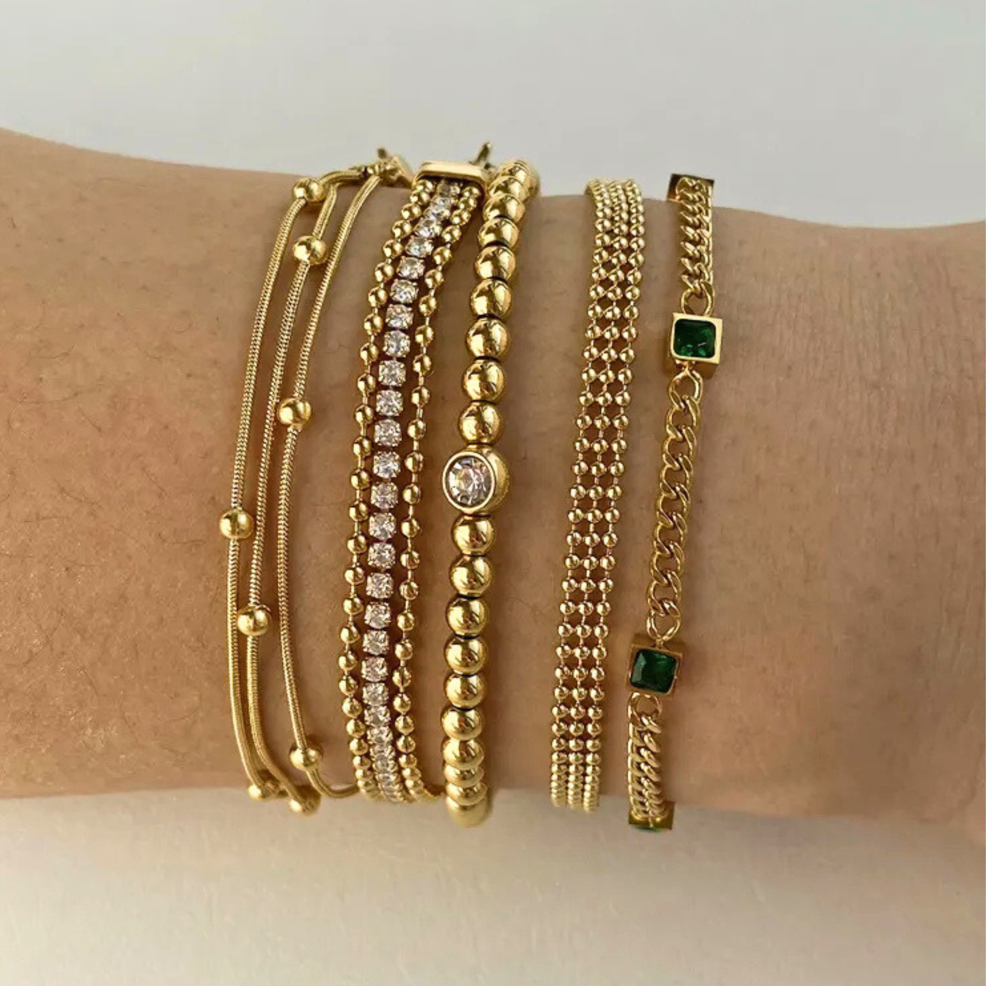 Gold bracelets on a wrist against a neutral background