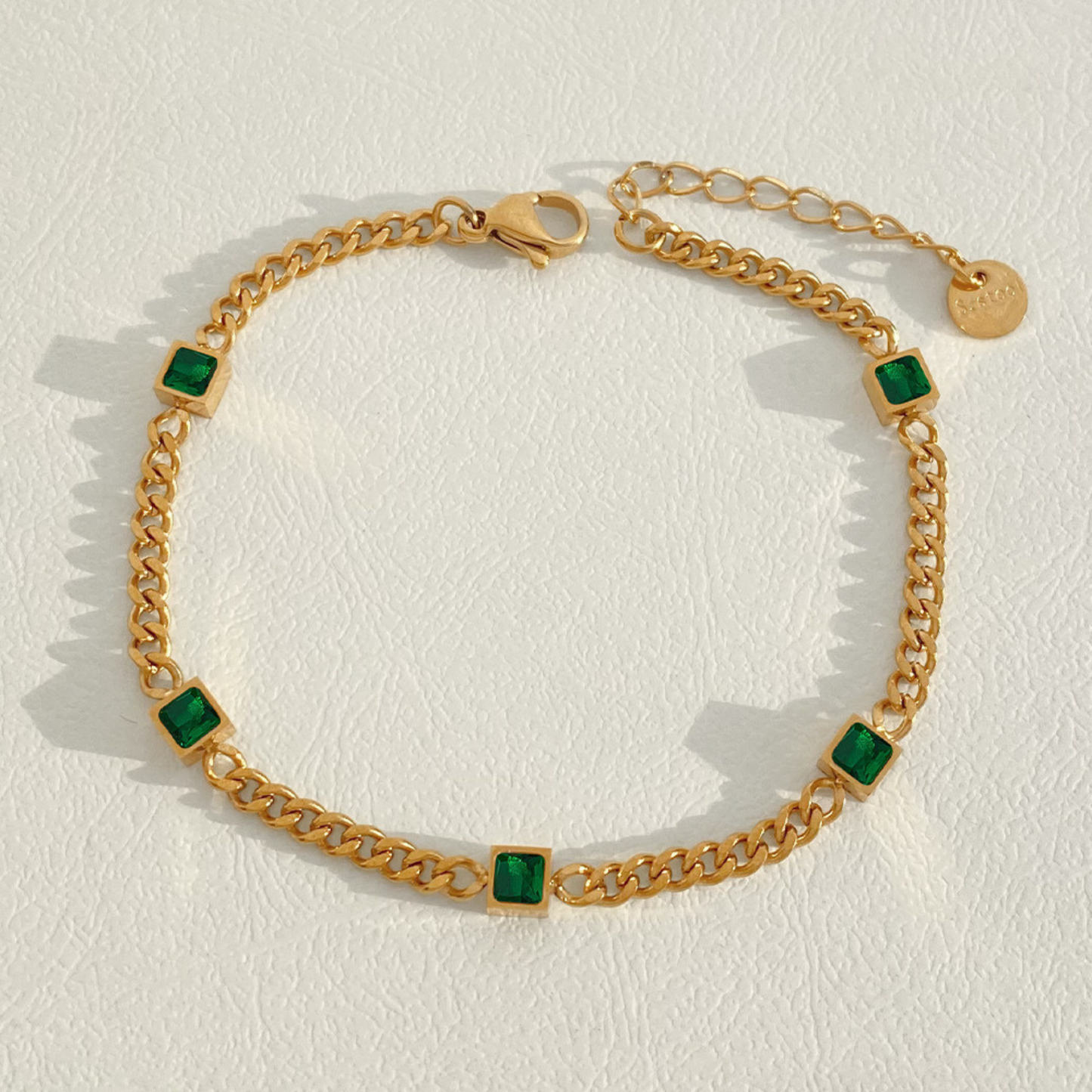 Gold chain bracelet with green square stones on a light background