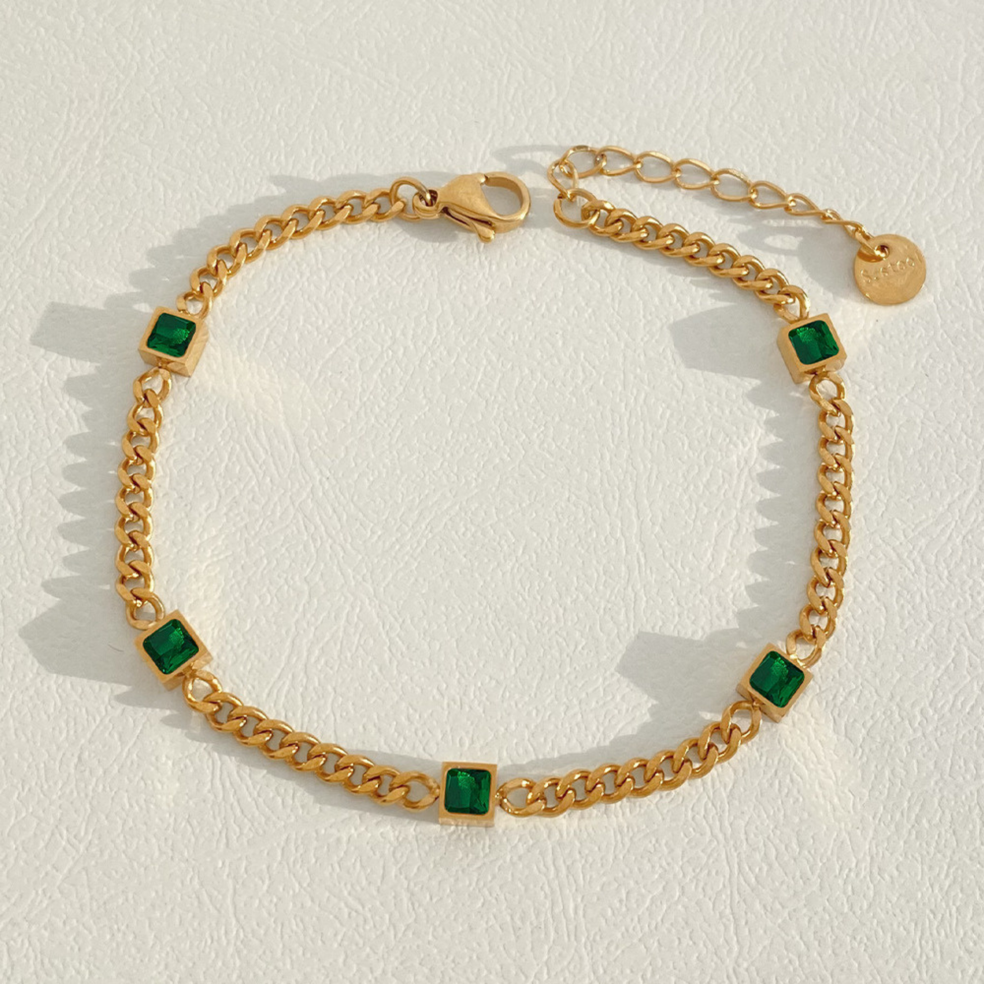 Gold chain bracelet with green square stones on a light background