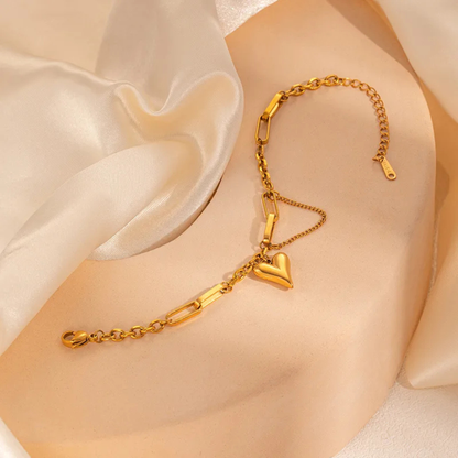 Gold bracelet with a heart charm on a soft beige fabric background