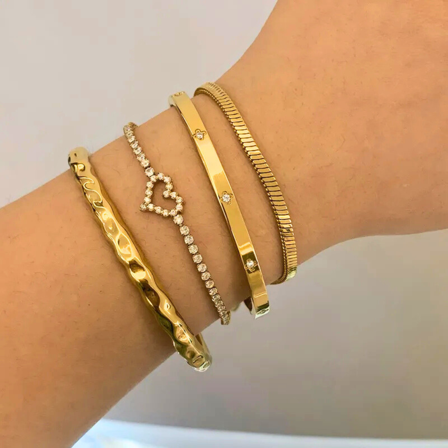 Gold bracelets on a wrist against a neutral background