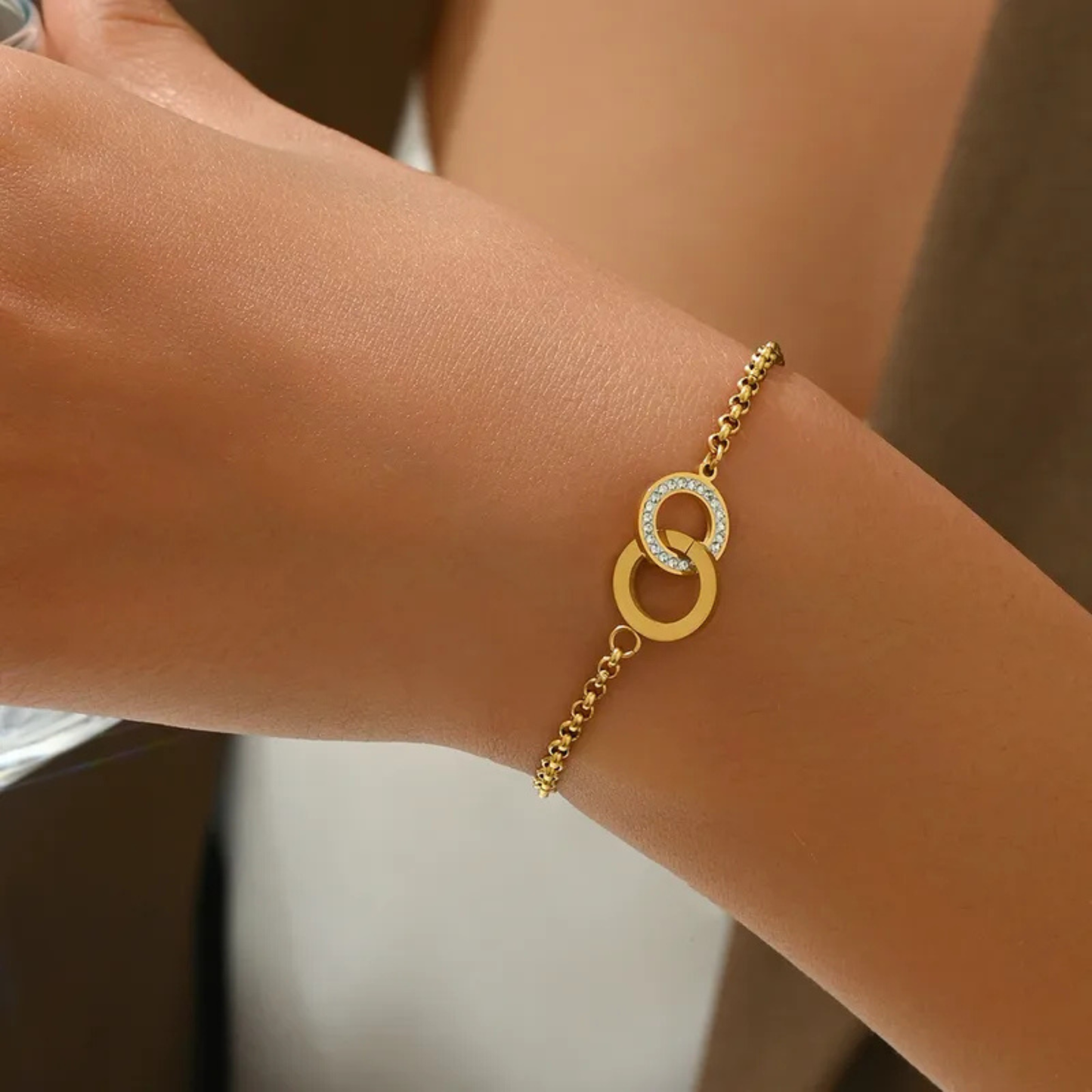 Gold bracelet with interlocking rings on a wrist against a neutral background