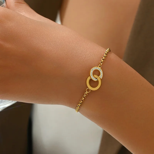 Gold bracelet with interlocking rings on a wrist against a neutral background