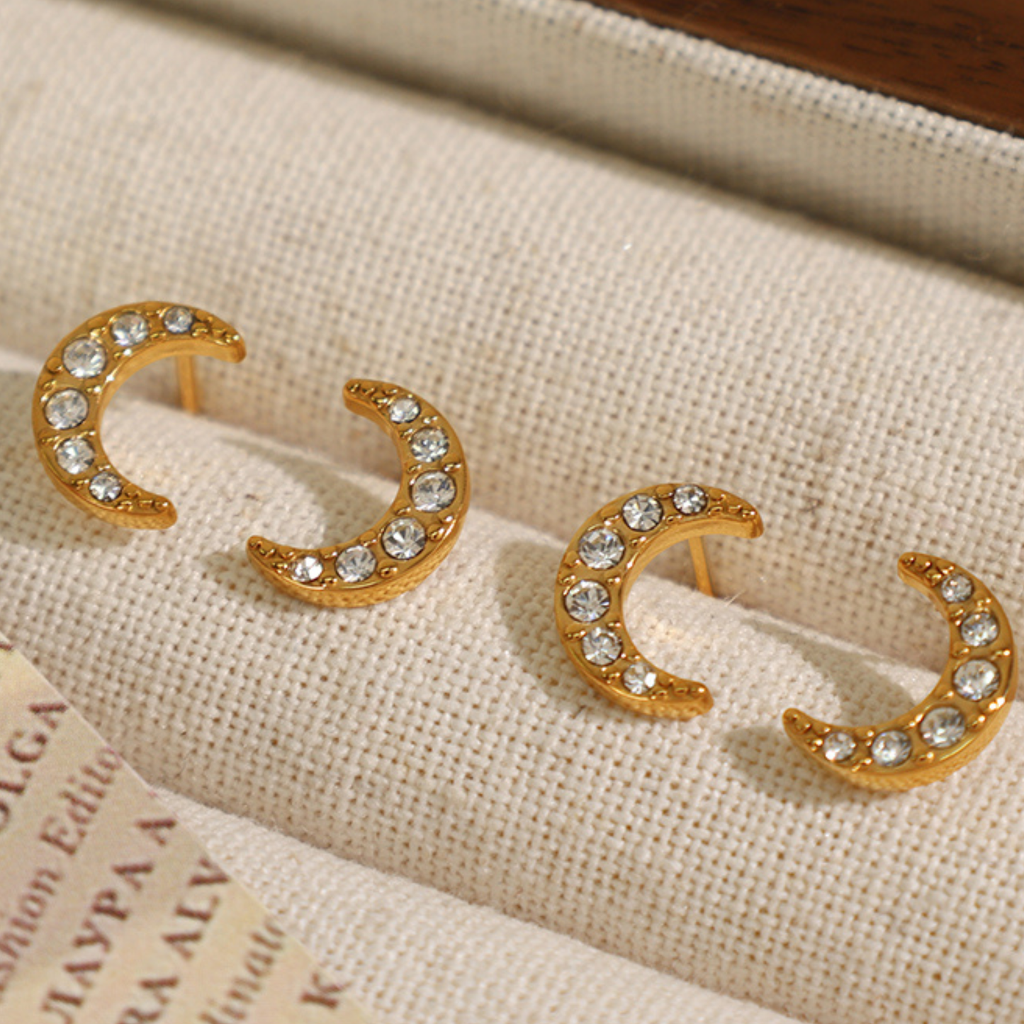 Gold crescent moon earrings with rhinestones on a textured fabric background