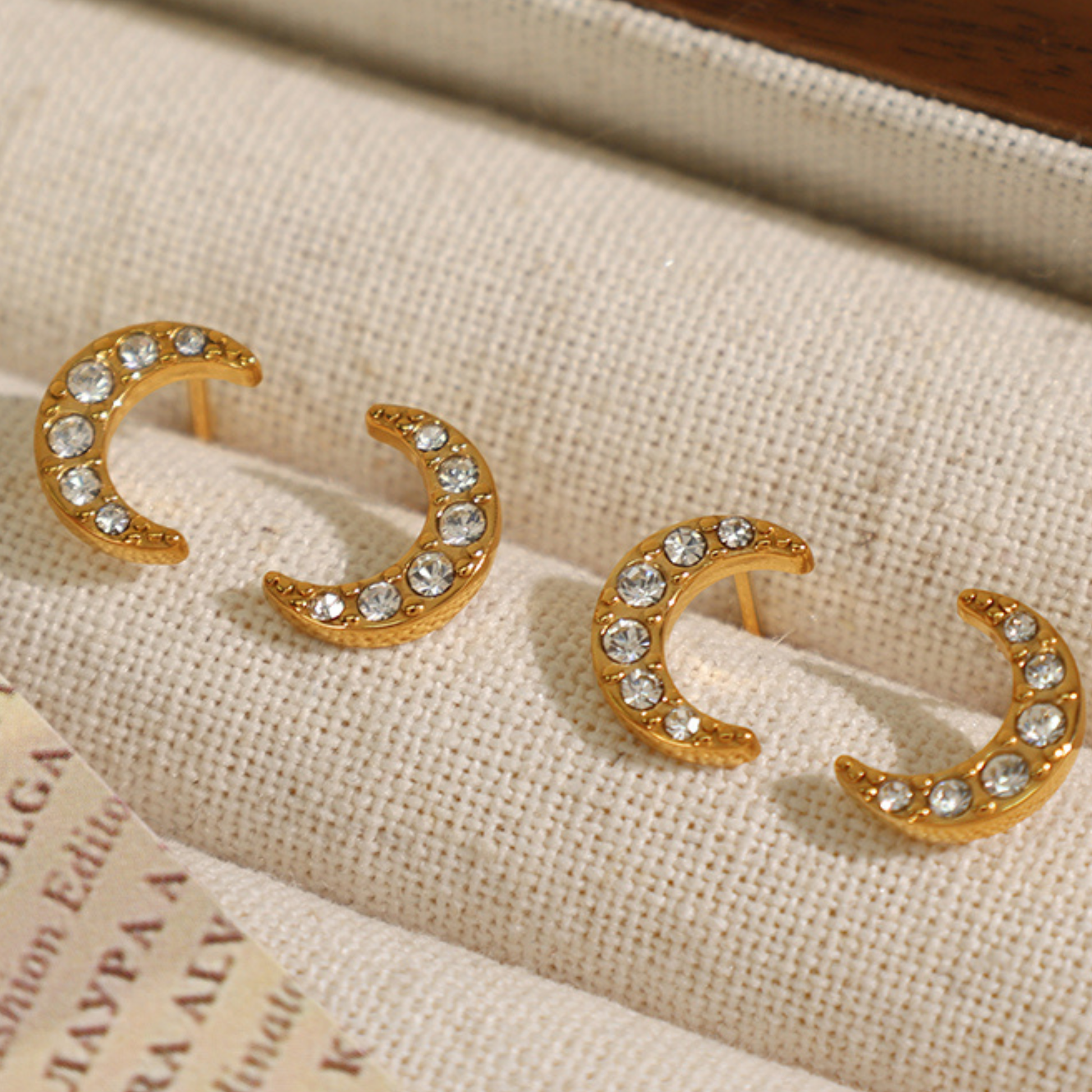 Gold crescent moon earrings with rhinestones on a textured fabric background