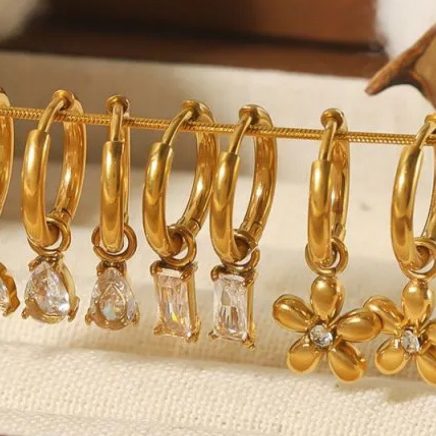 Gold hoop earrings with various gemstone pendants on a textured surface