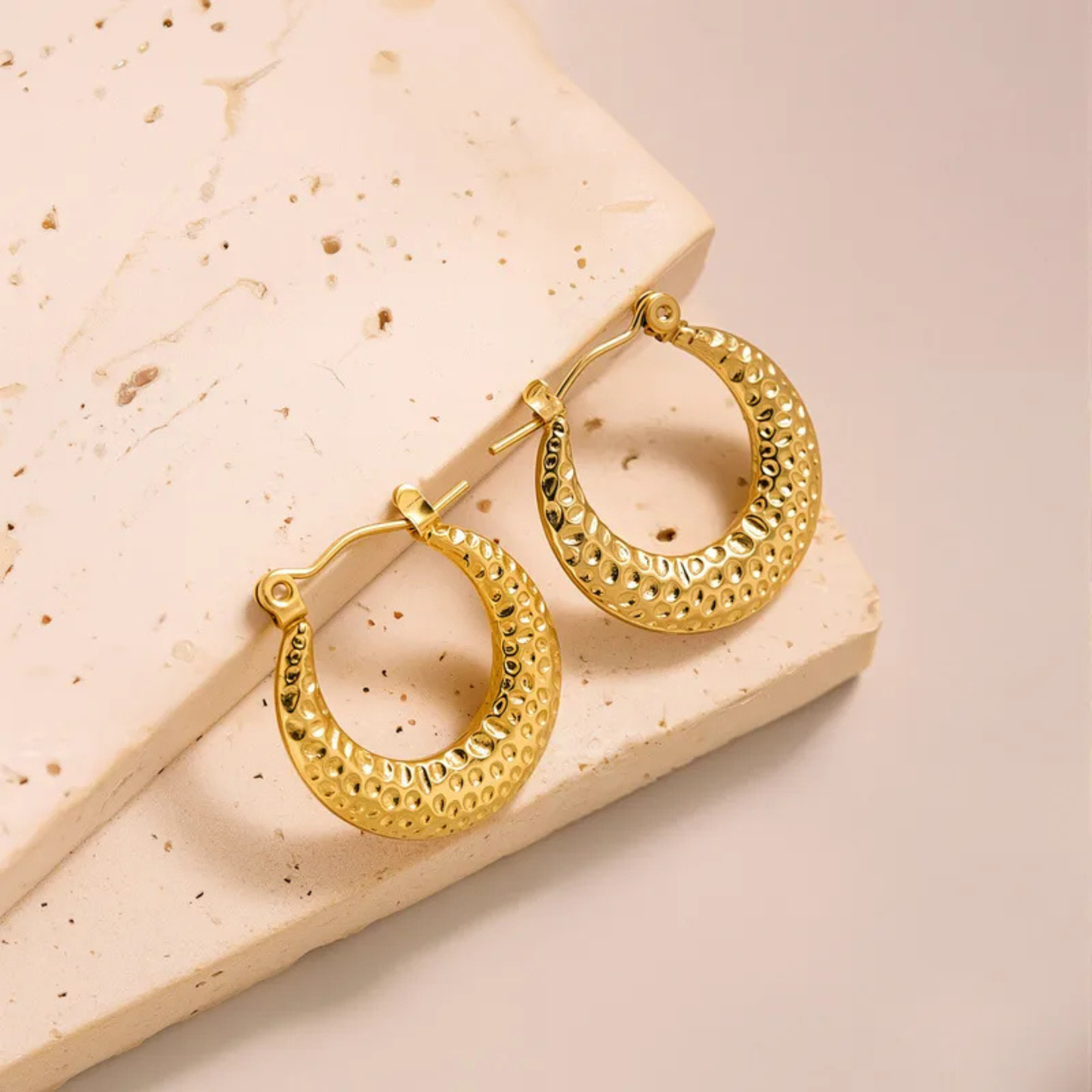 Gold hoop earrings on a textured beige surface