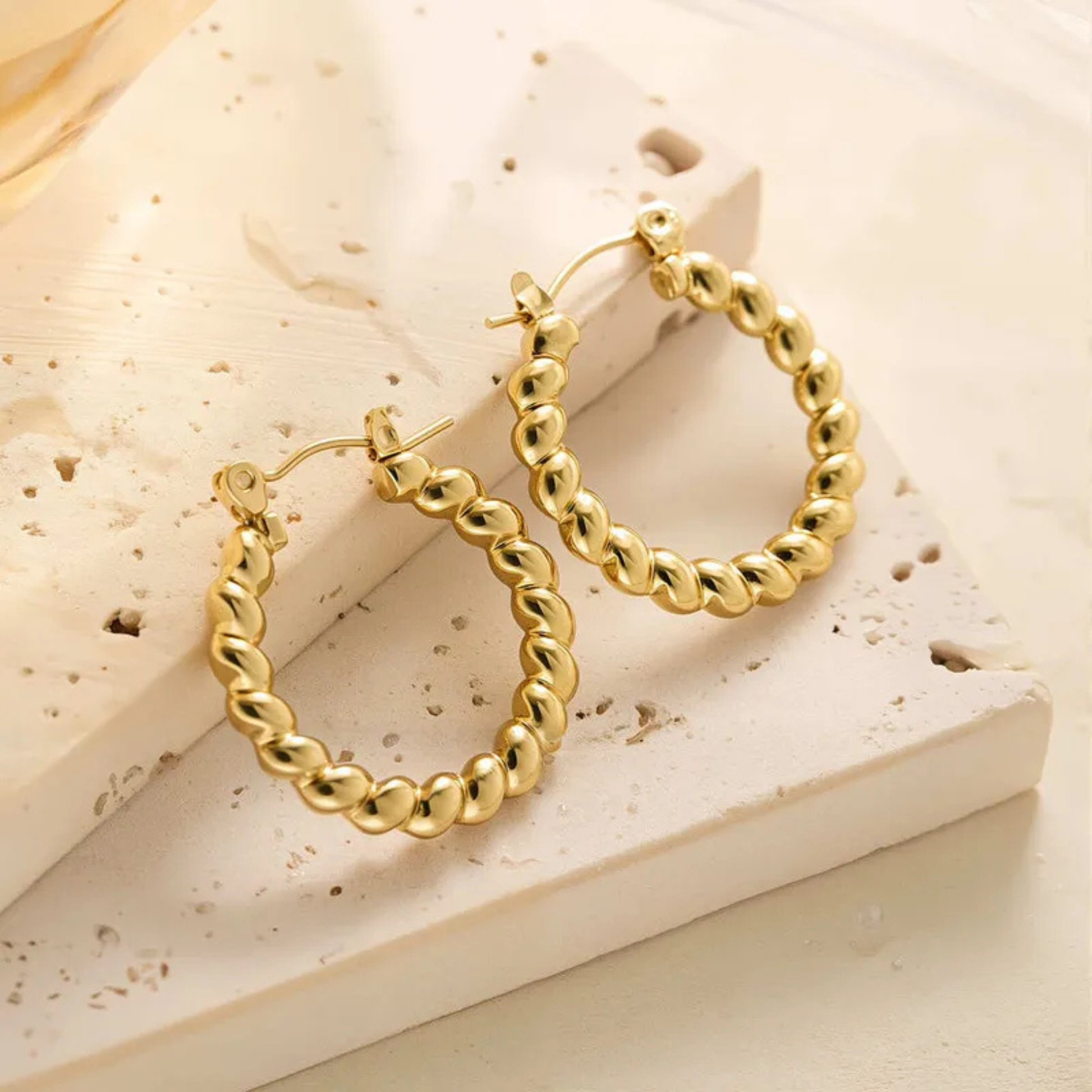 Gold hoop earrings on a textured beige surface