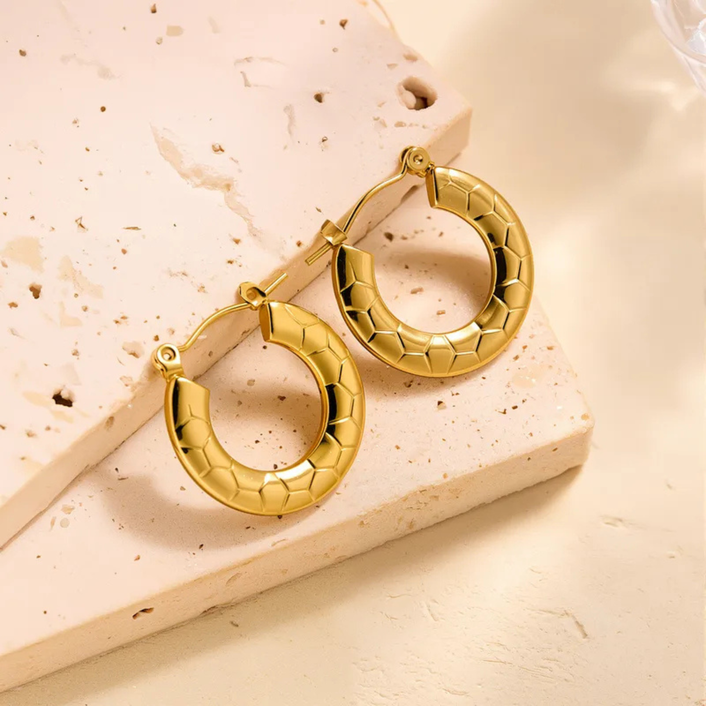 Gold hoop earrings on a textured beige surface
