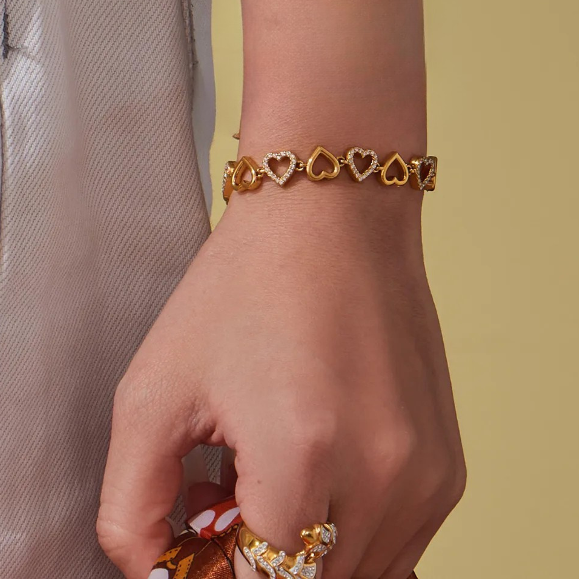 Gold bracelet with heart designs on a wrist against a neutral background