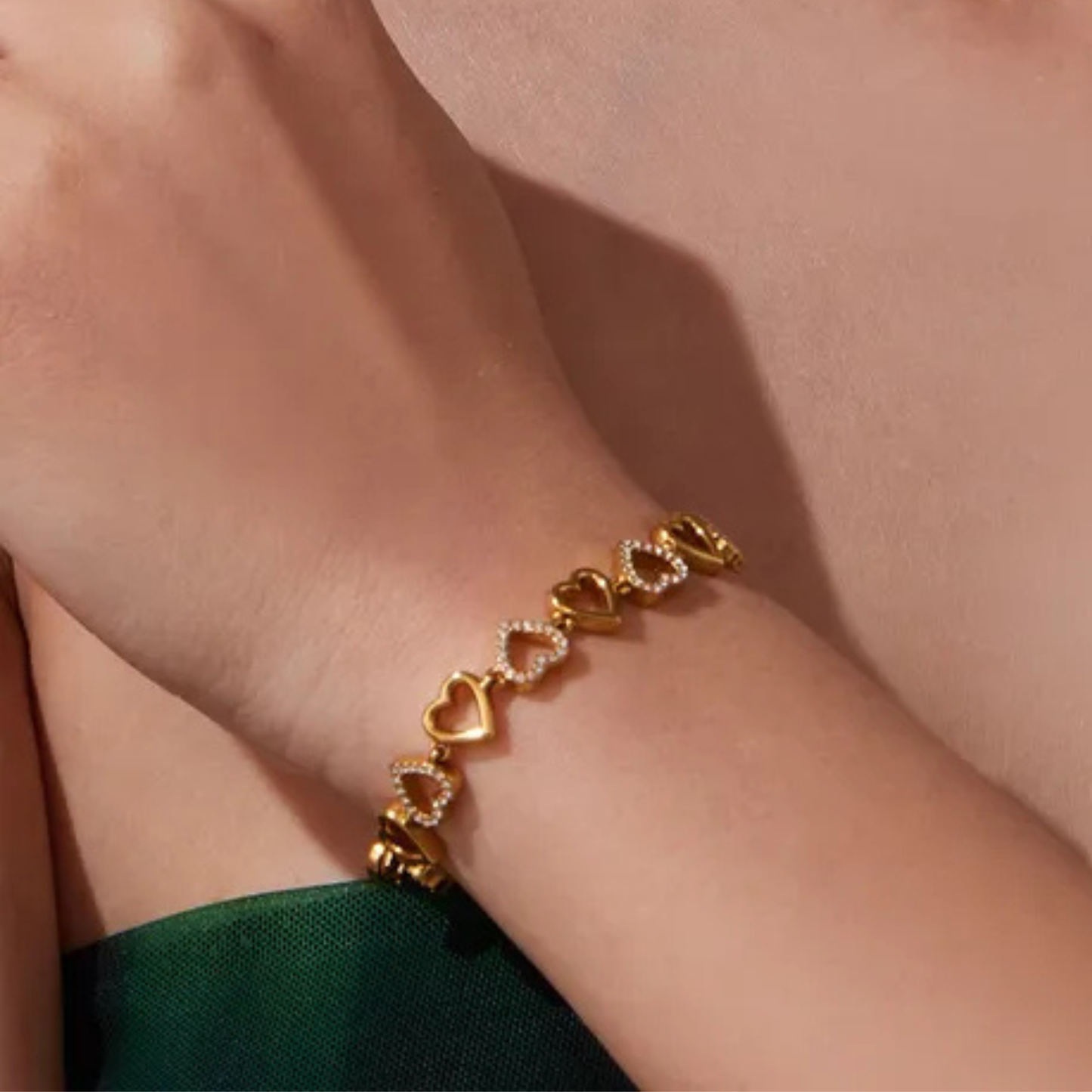 Gold bracelet with heart-shaped links on a wrist against a neutral background