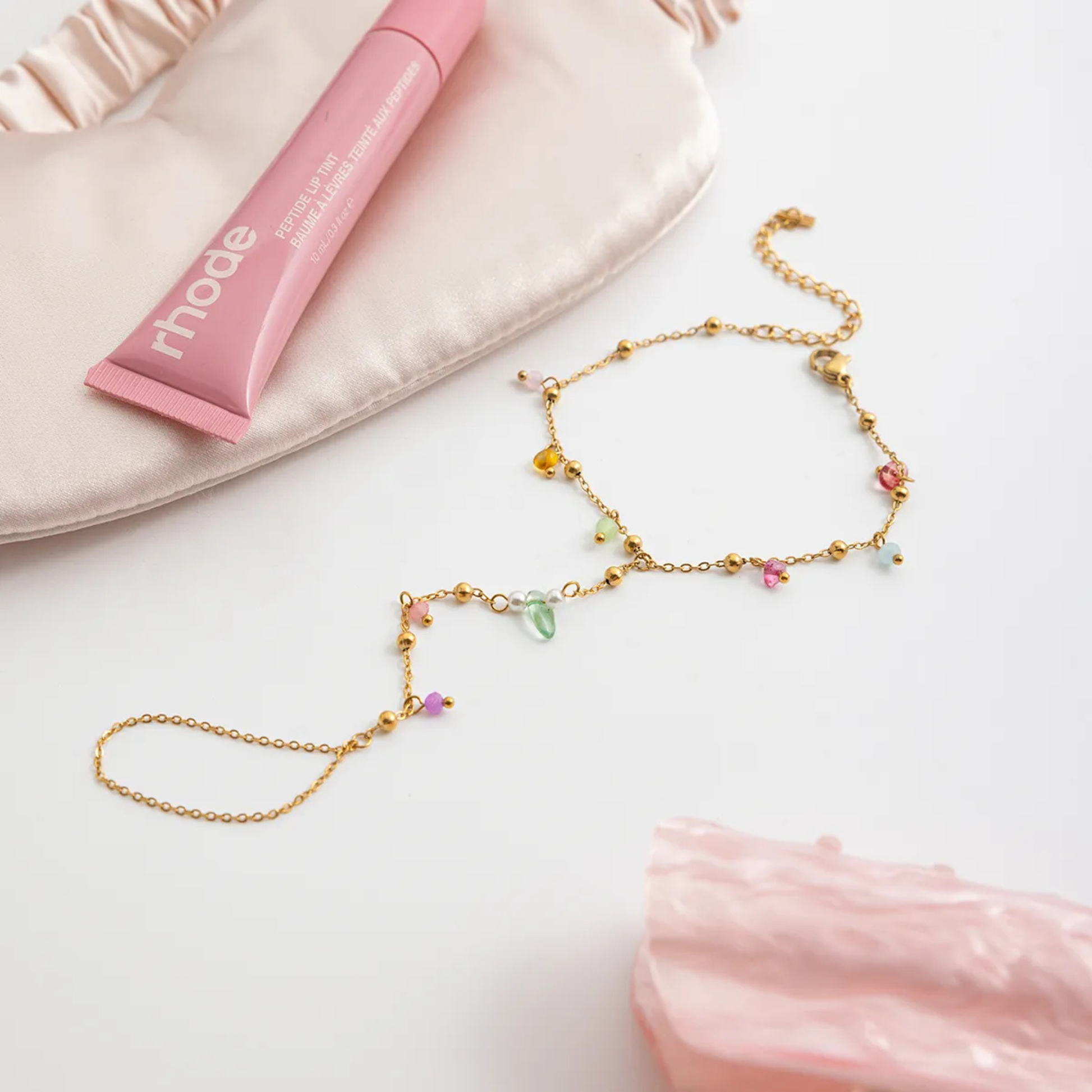 Gold necklace with colorful beads on a white surface with pink jewelry box and pillow.