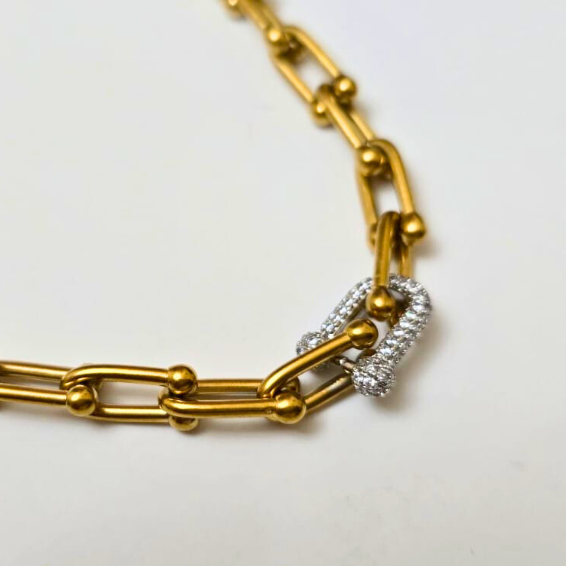 Gold chain bracelet with a silver heart charm on a light background
