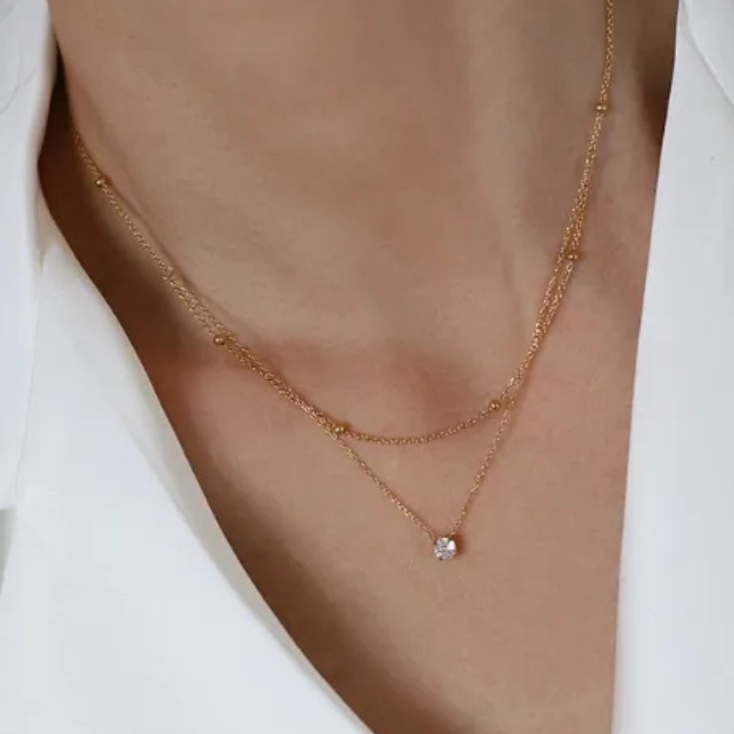 Gold necklace with a small pendant on a person wearing a white shirt.