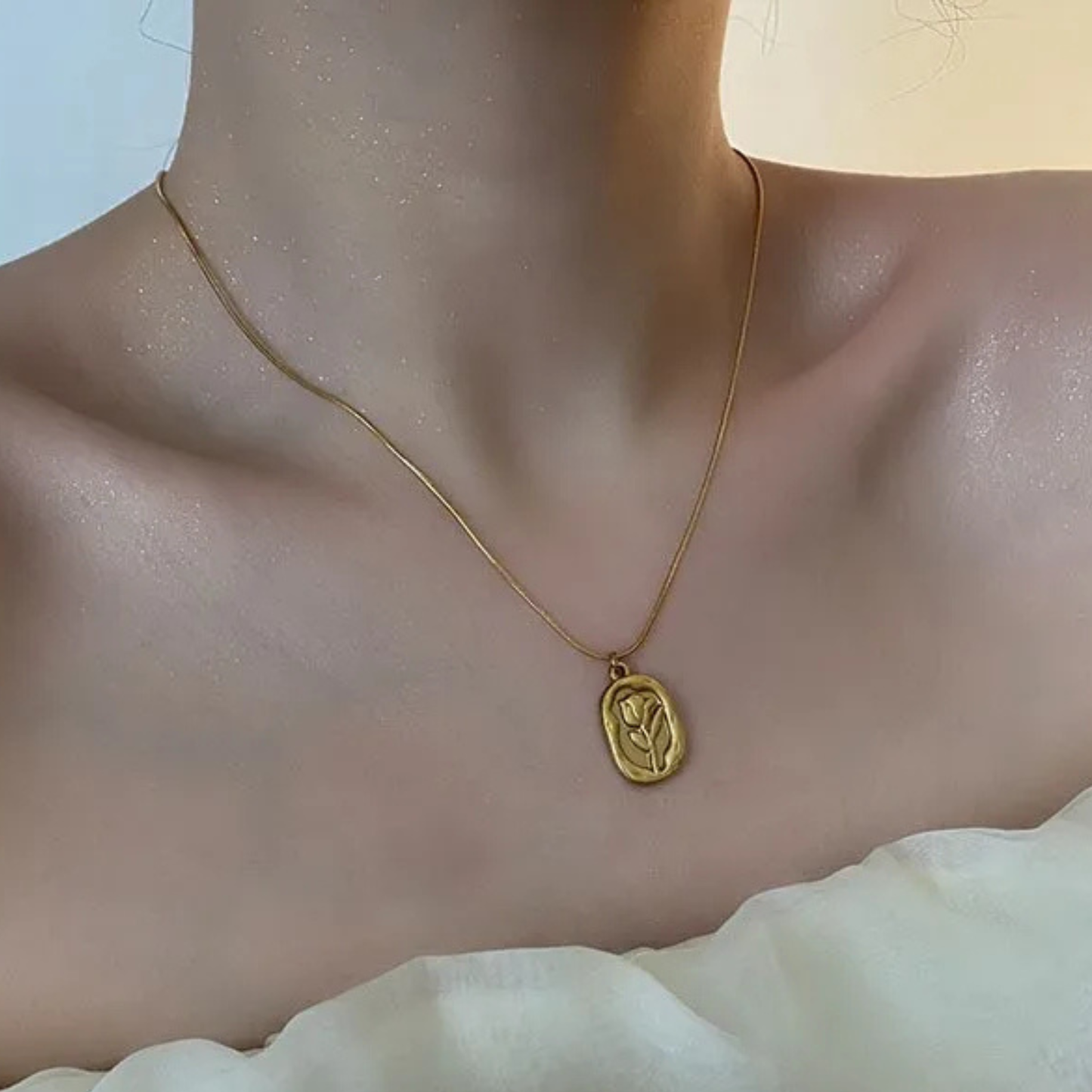 Gold necklace with a pendant on a person wearing a white garment.